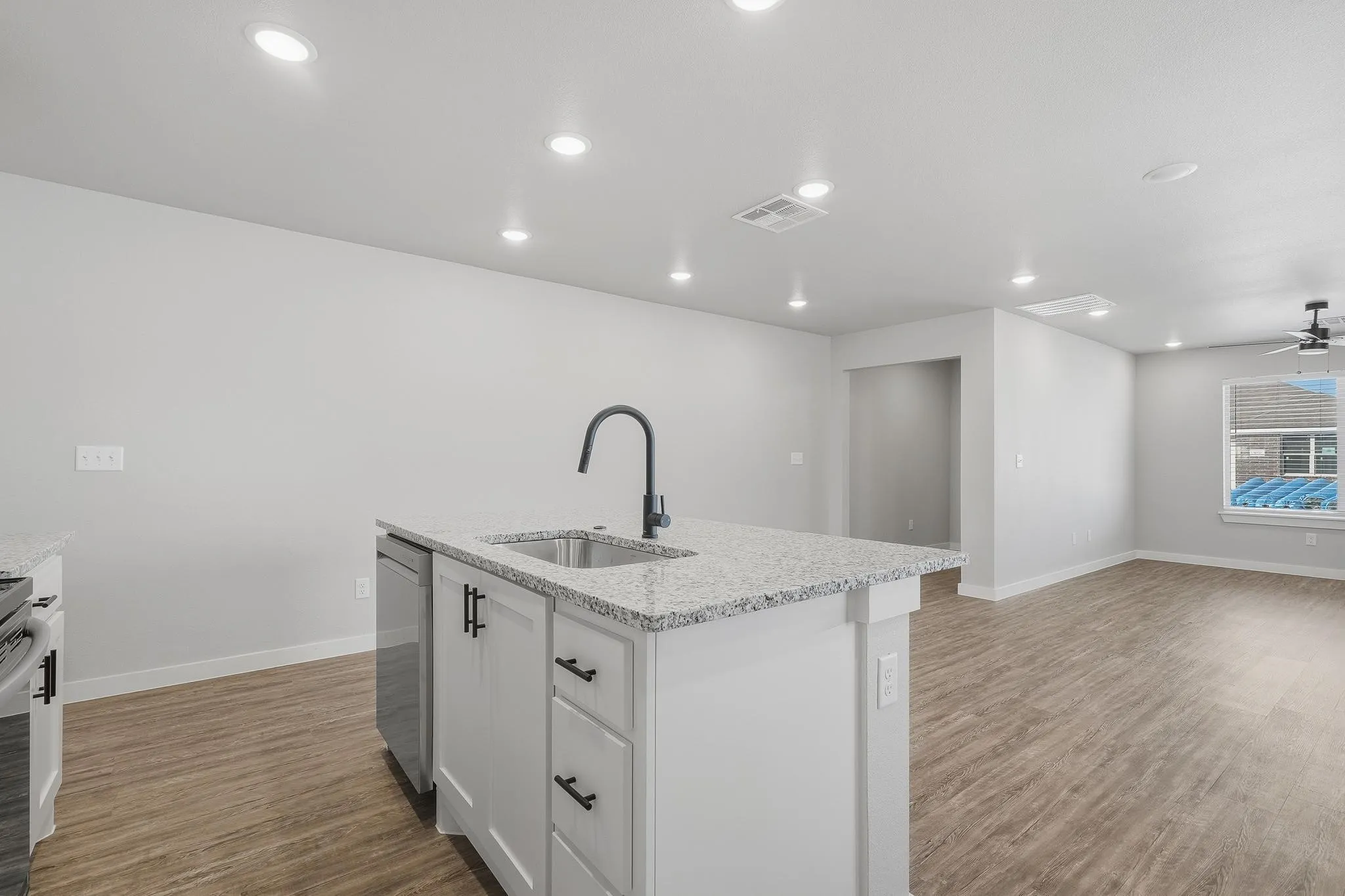 Kitchen island featuring a single-basin sink with a matte black faucet, granite-style countertop, and white shaker-style cabinetry with black hardware