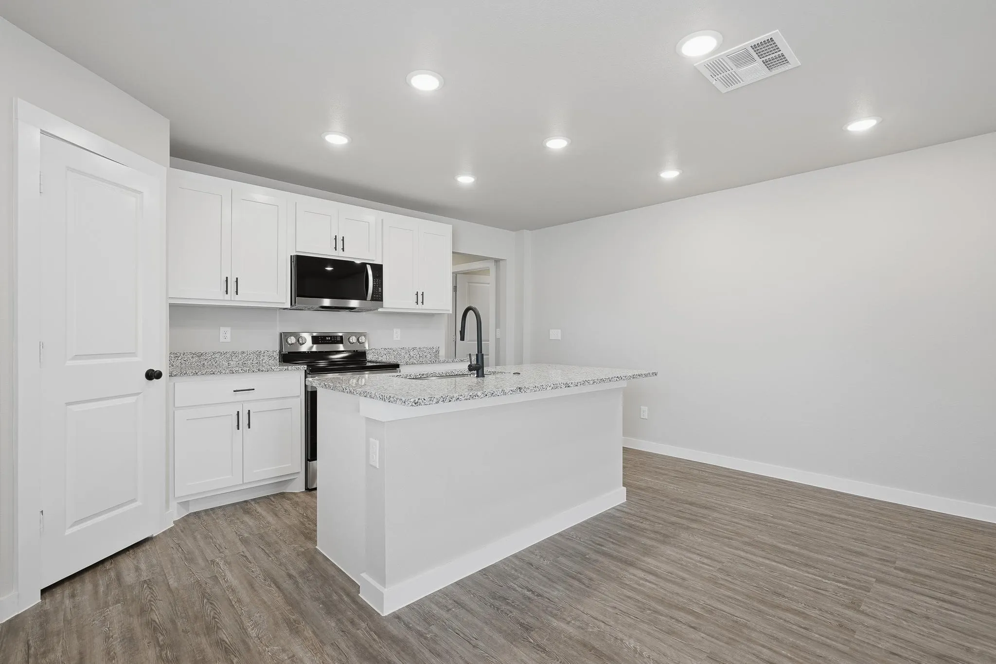 Modern kitchen space featuring white shaker cabinetry, stainless steel appliances, granite countertops, and an island with a breakfast bar