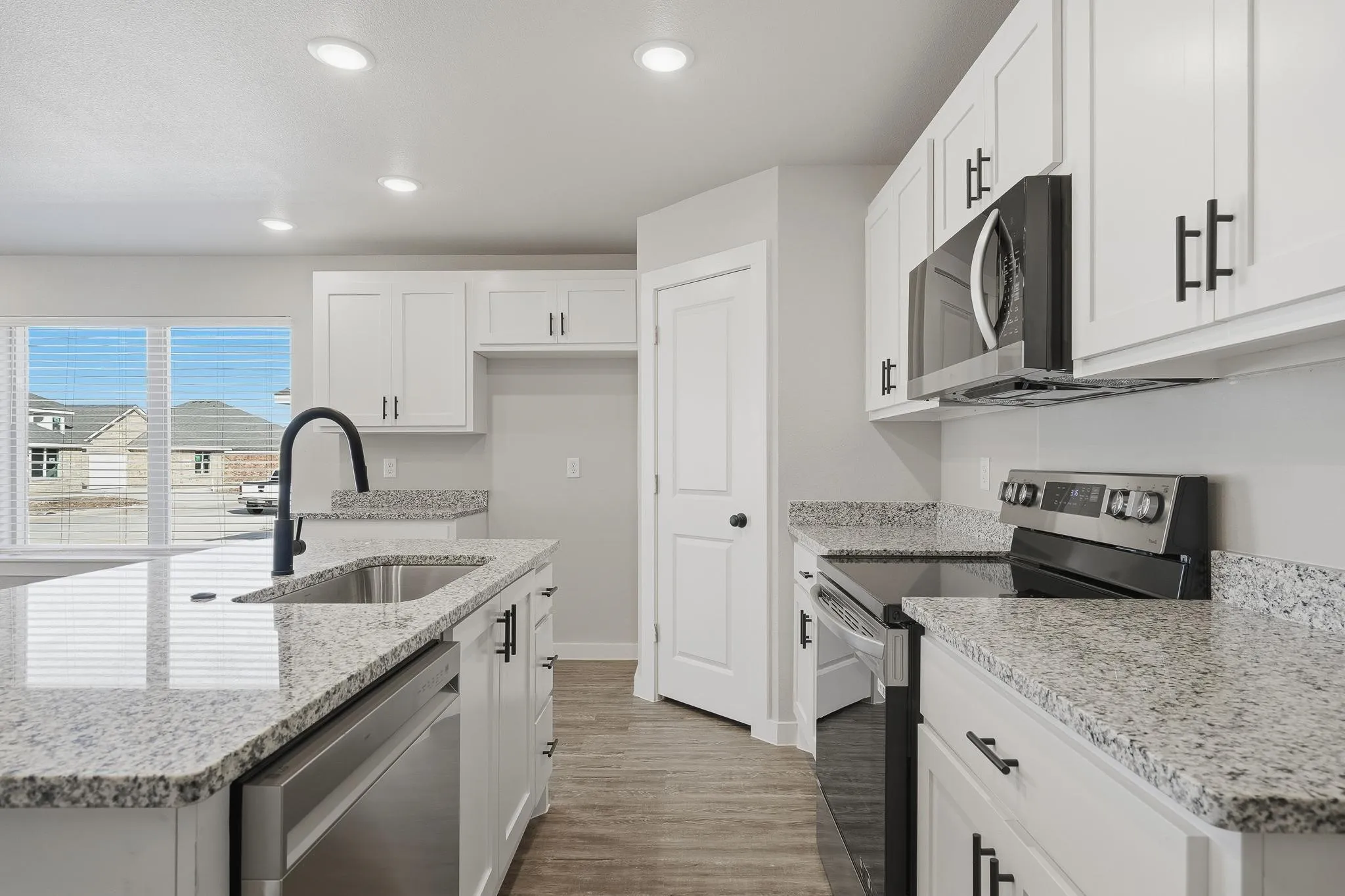 Modern kitchen featuring white cabinetry, granite countertops, stainless steel appliances, a kitchen island with sink and a matte black faucet, and wood-finish flooring