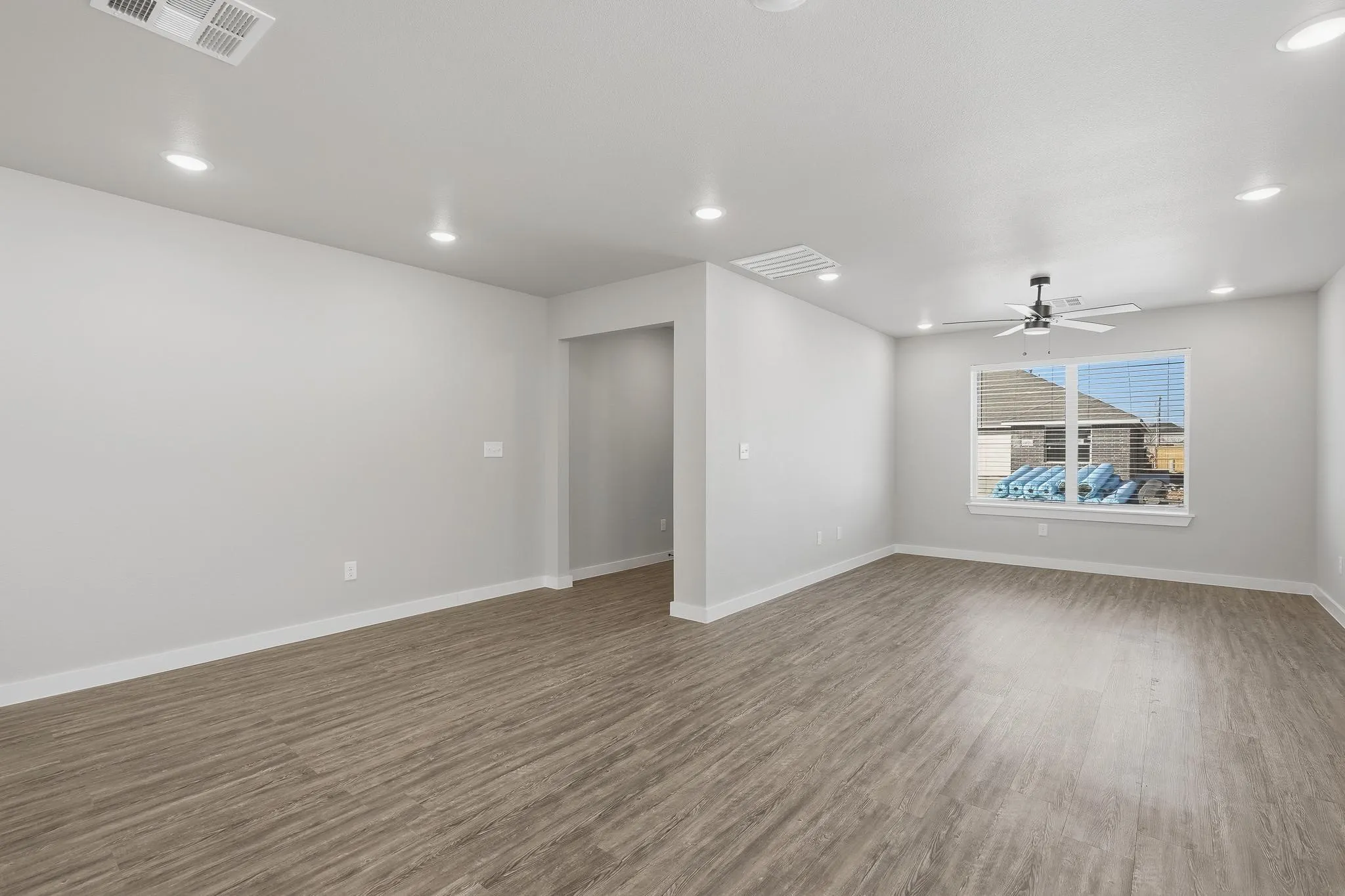 Spacious interior room featuring wood-finish flooring, recessed lighting, and a ceiling fan with integrated lighting