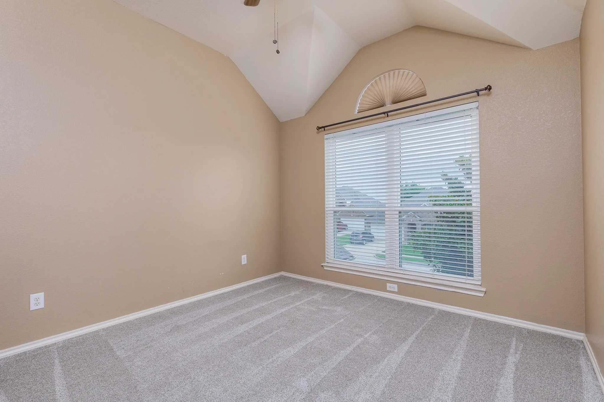 Vaulted ceiling room featuring a large window with blinds, an arched transom window, and grey patterned carpet