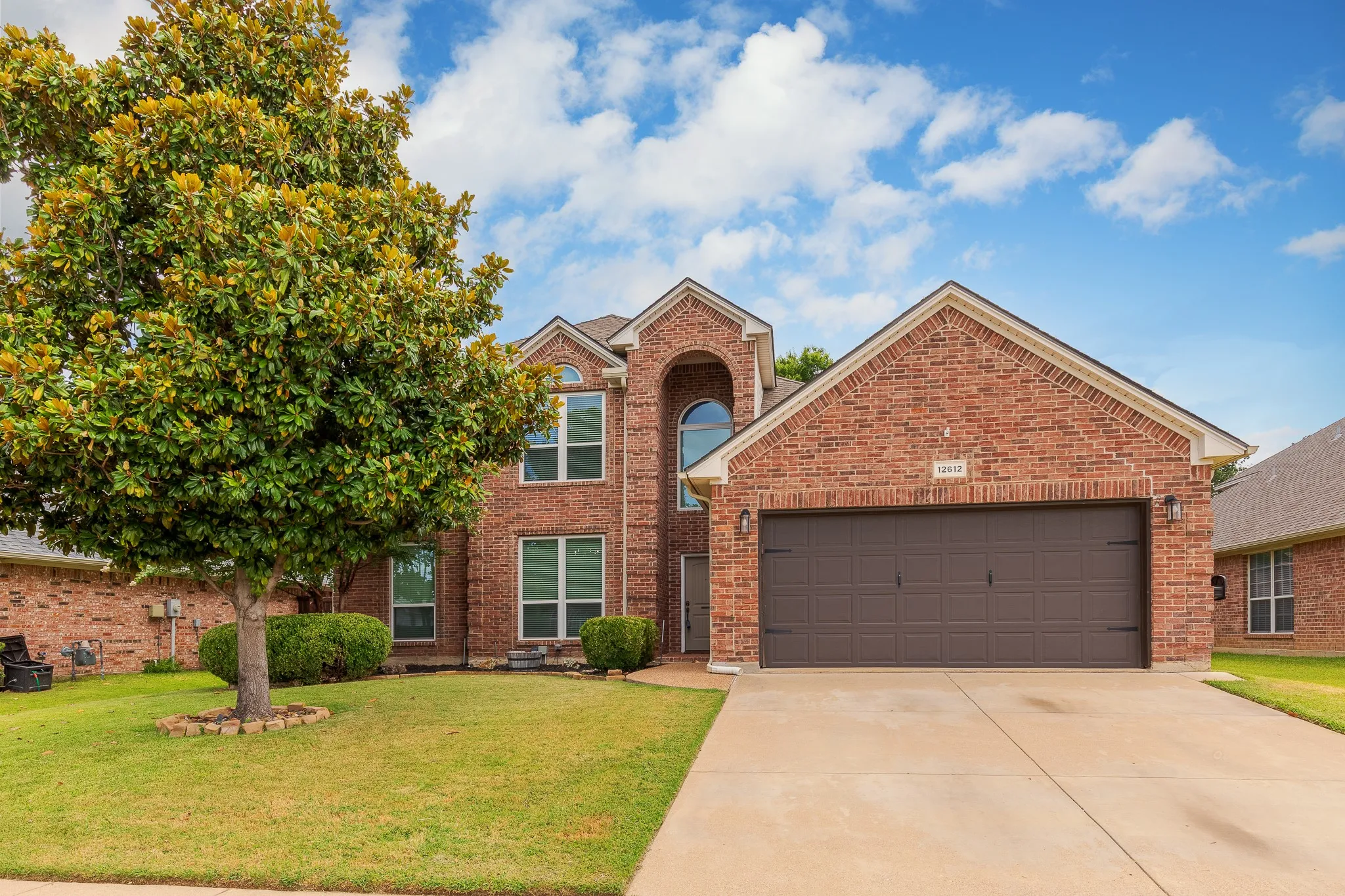 Brick facade residence featuring a two-car garage with a panel door, arched entryway, and multiple windows