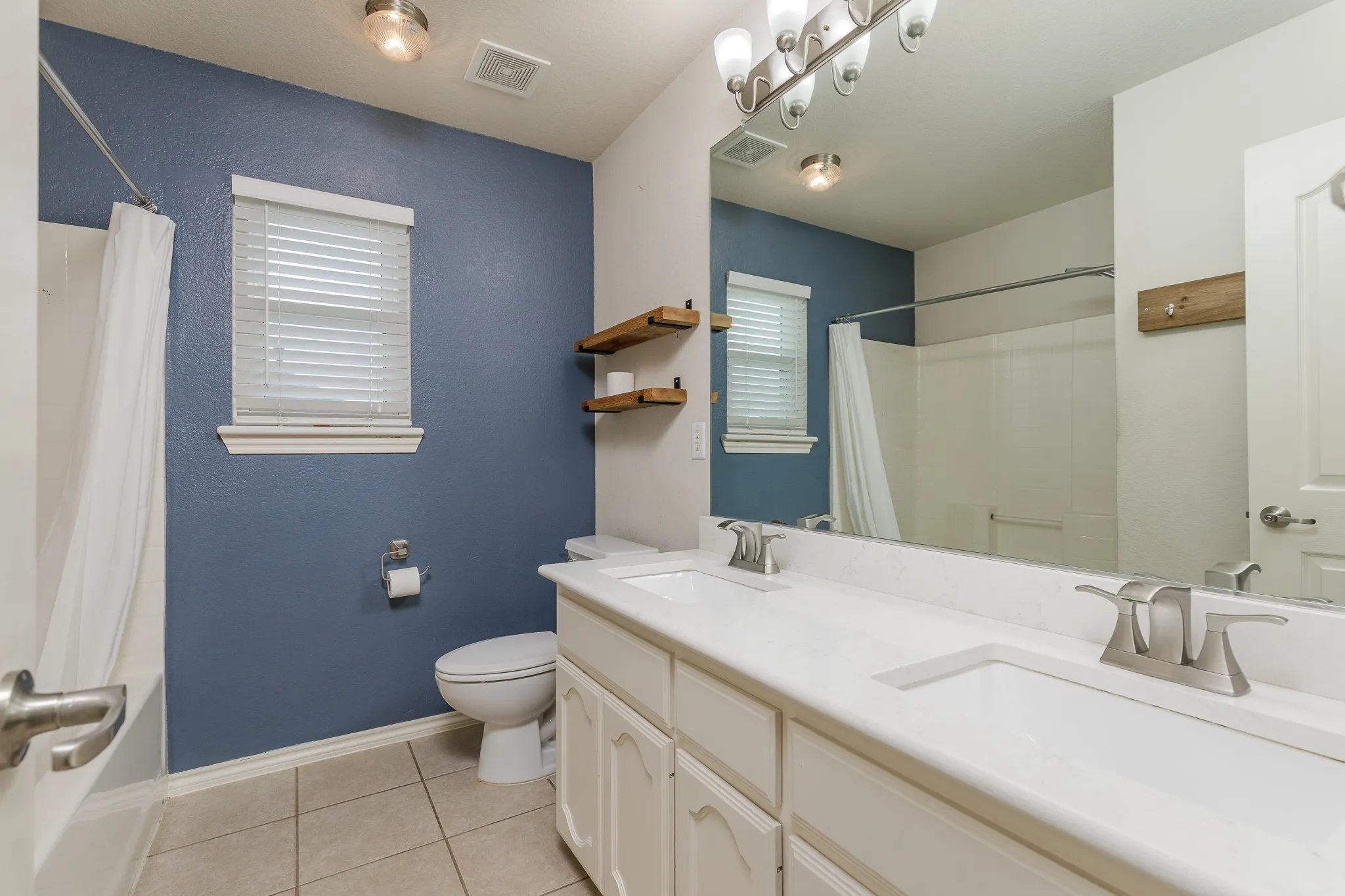 Bathroom featuring a double vanity with integrated sinks, brushed nickel fixtures, and a large wall-mounted mirror