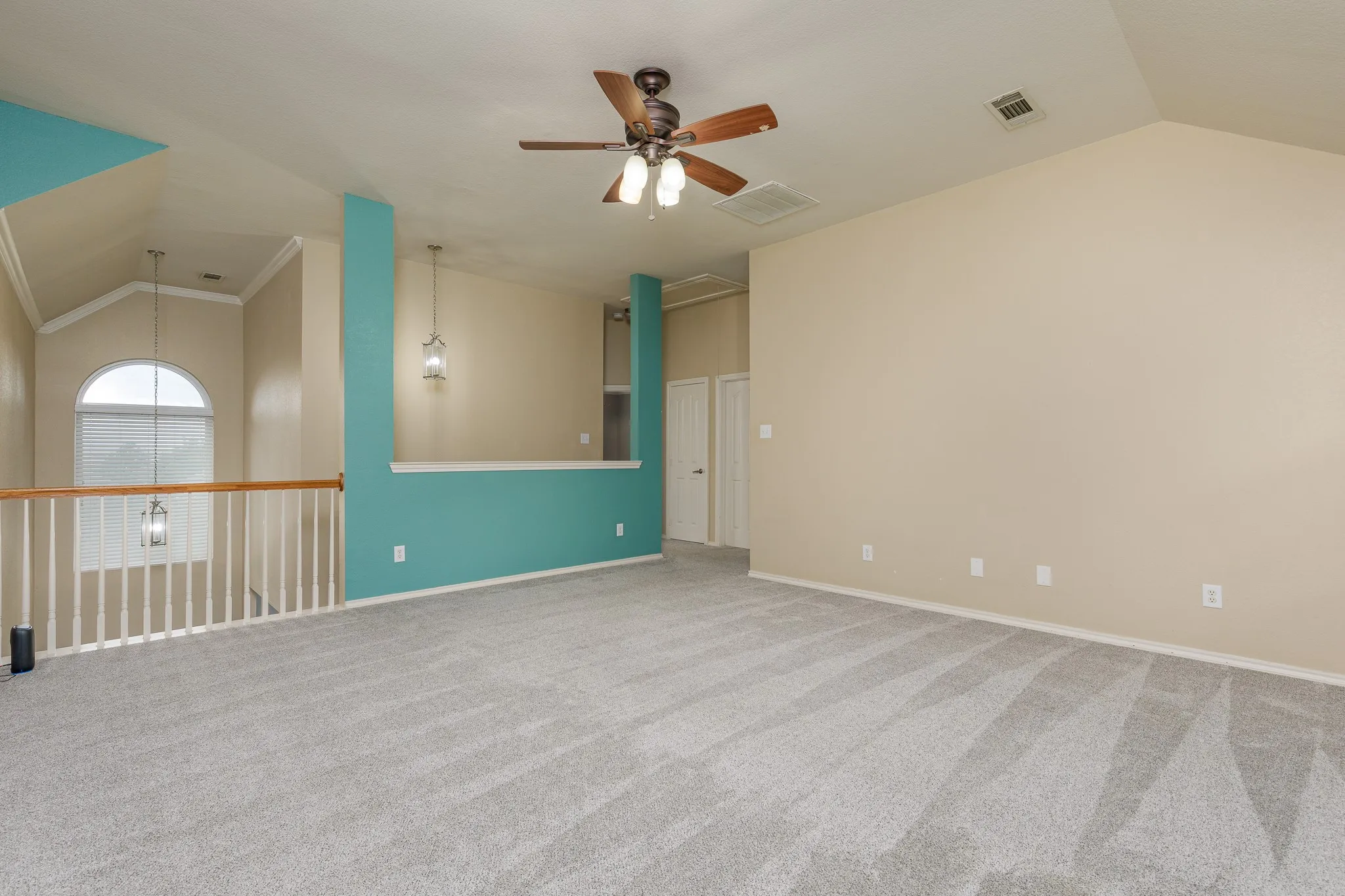 Spacious loft area featuring vaulted ceilings, light gray carpeting, and a ceiling fan with integrated lighting