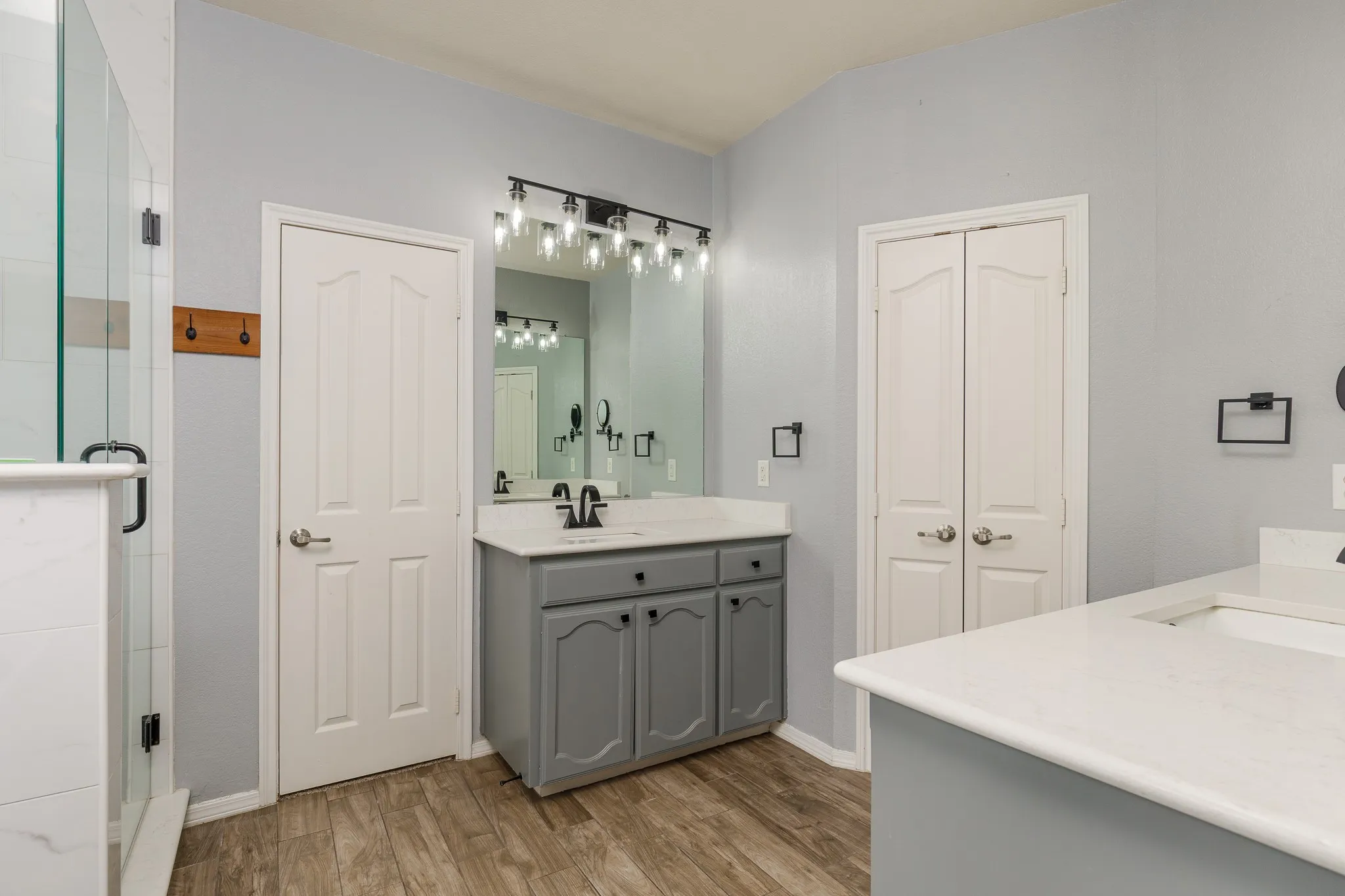 Bathroom featuring a double vanity with grey cabinetry, white countertops, and wood-finish flooring