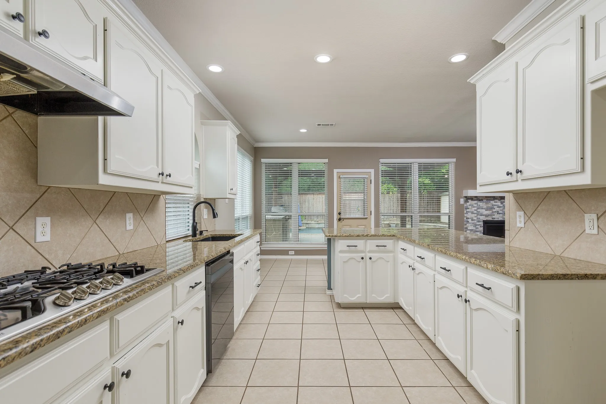 Expansive kitchen featuring white cabinetry, stone countertops, stainless steel appliances, and a tiled backsplash