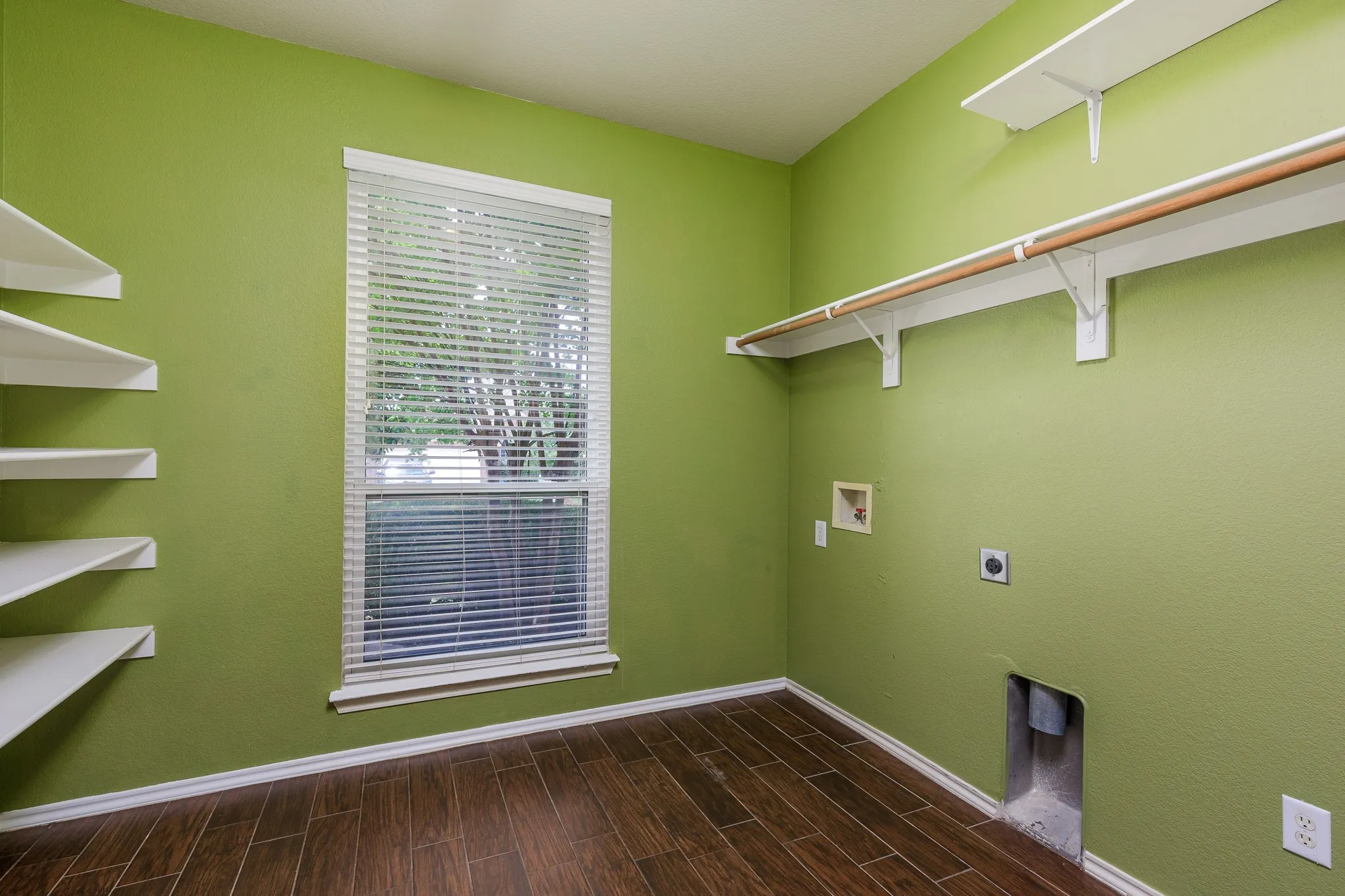 Utility room featuring wood-finish flooring, a window with blinds, built-in shelving, a clothes rod, and appliance hookups