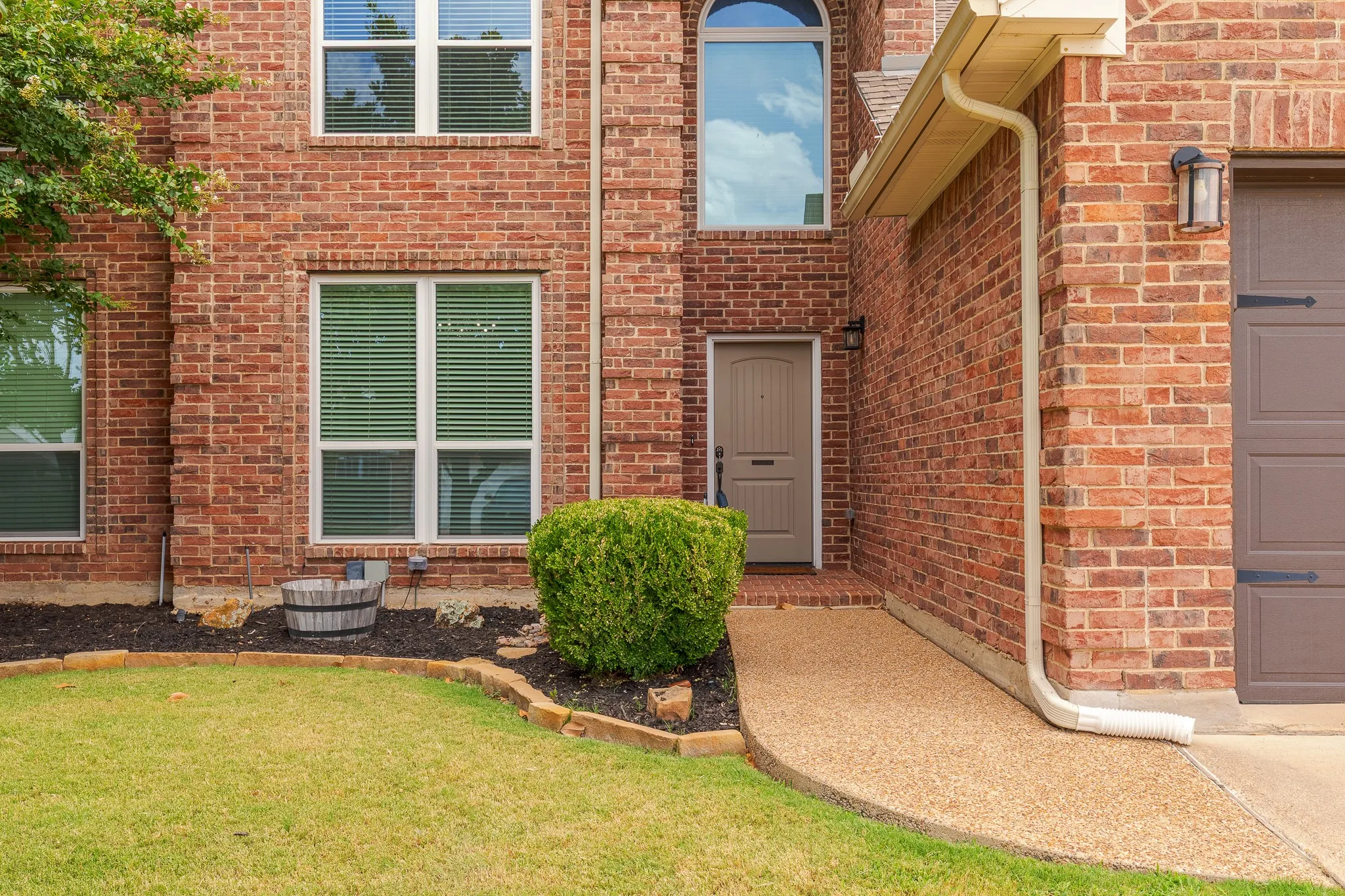 Brick facade residence featuring a front entry door, arched window, and attached garage