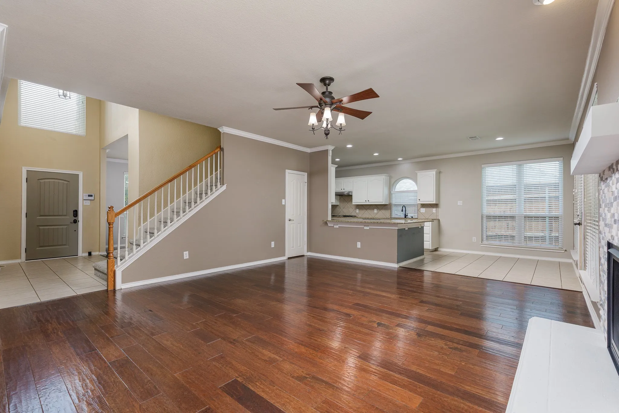 Open-concept living area featuring wood-finish flooring, a contemporary ceiling fan, and a kitchen with white cabinetry, a breakfast bar, and a tiled​​‌​​​​‌​​‌‌​‌‌​​​‌‌​‌​‌​‌​​​‌​​ backsplash