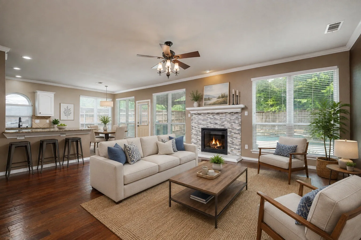 Open-concept living space featuring hardwood flooring, a gas fireplace with tile surround, ceiling fan with integrated lighting, and expansive windows with natural light