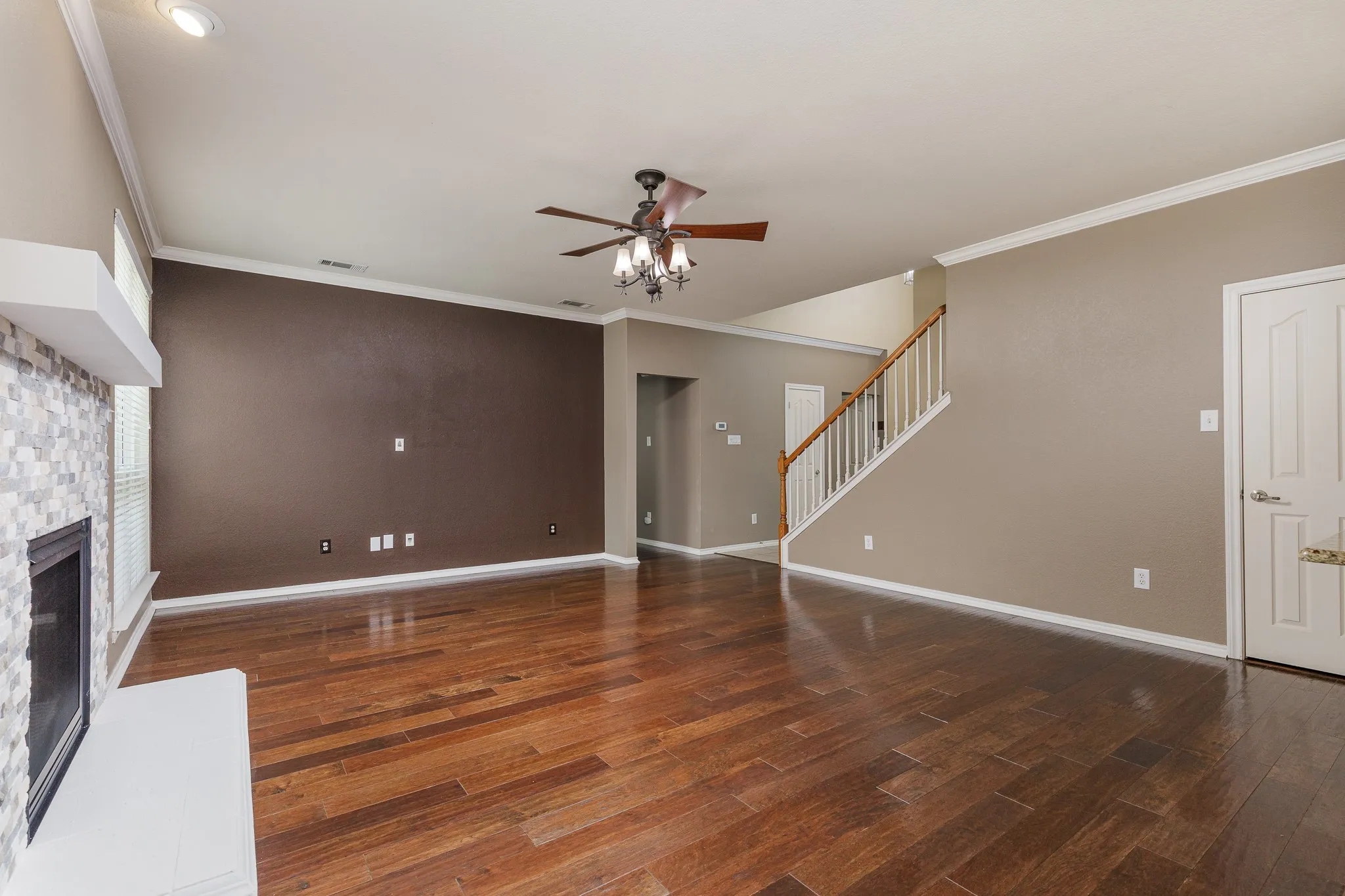 Spacious living area featuring rich wood-finish flooring, a contemporary fireplace with a floating mantle, and a ceiling fan with integrated lighting