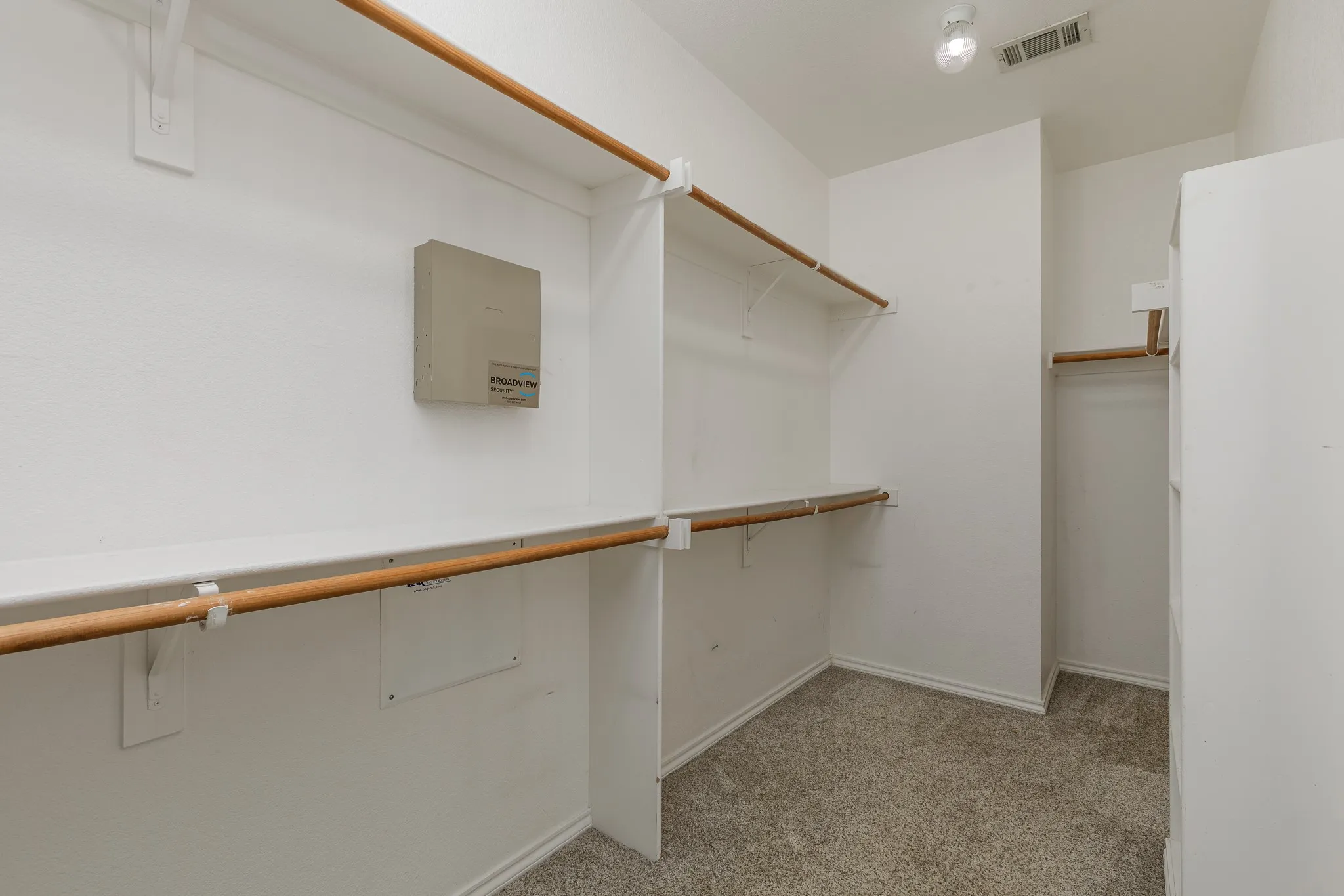 Spacious walk-in closet featuring white shelving with wood-finish rods, light gray carpet, and white walls