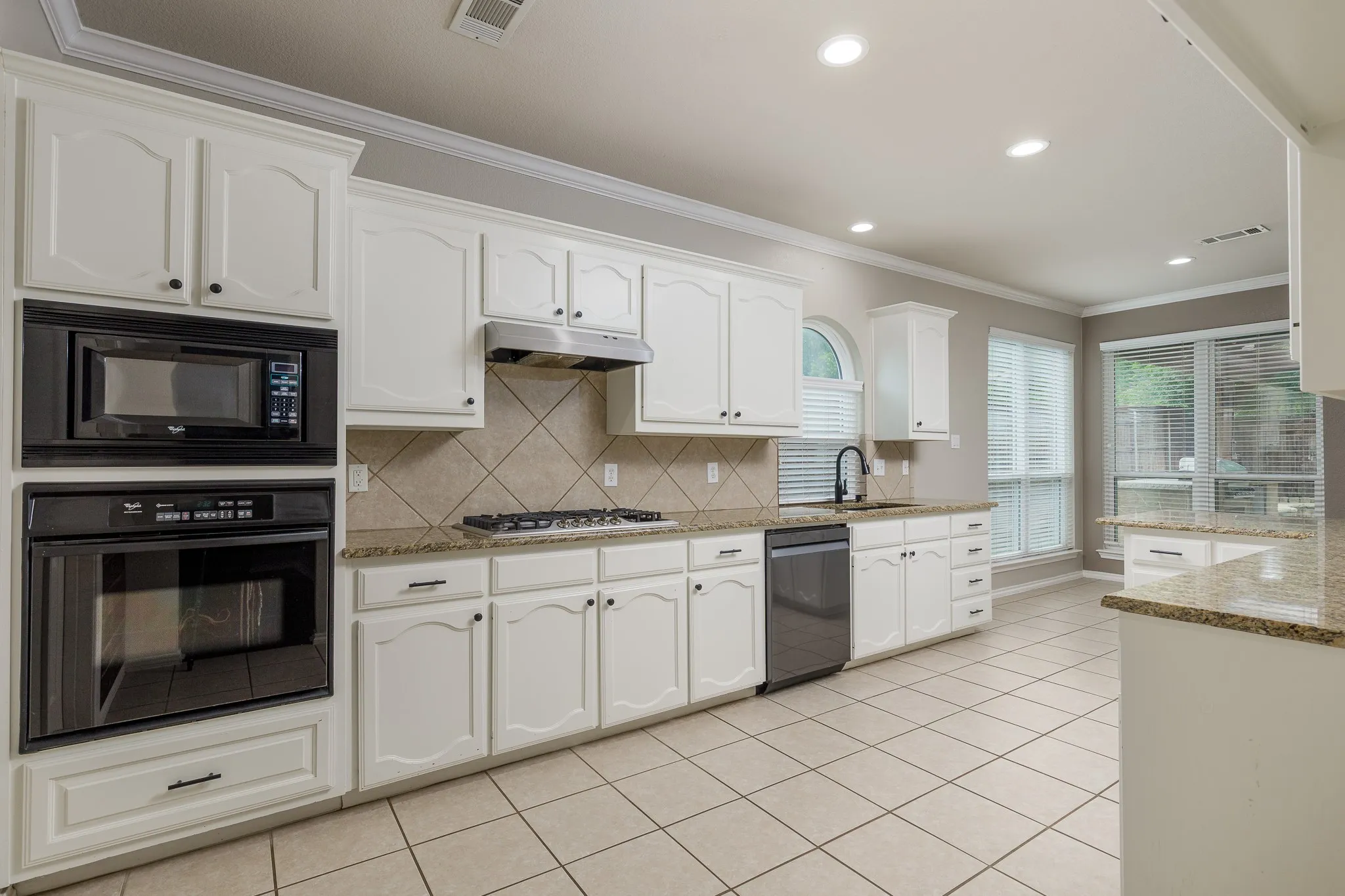 Bright kitchen featuring white cabinetry, granite countertops, tile backsplash, stainless steel gas range, and built-in microwave and oven