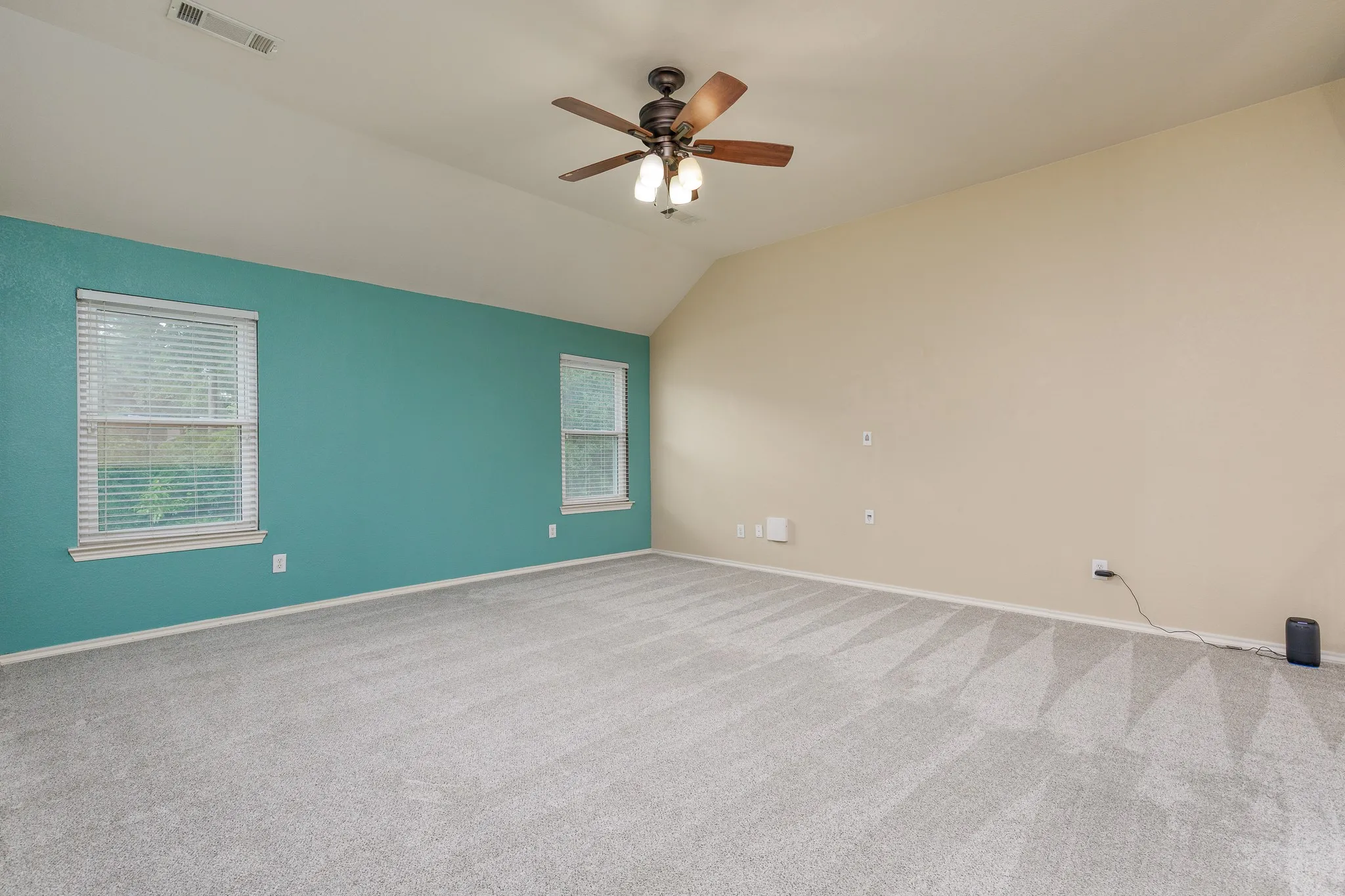 Spacious room featuring vaulted ceilings, light gray carpet, and two windows with blinds