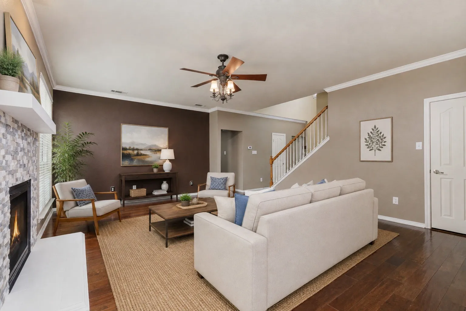 Spacious open-concept living area featuring a cream upholstered sectional sofa, wood-finish flooring, and a ceiling fan with integrated lighting