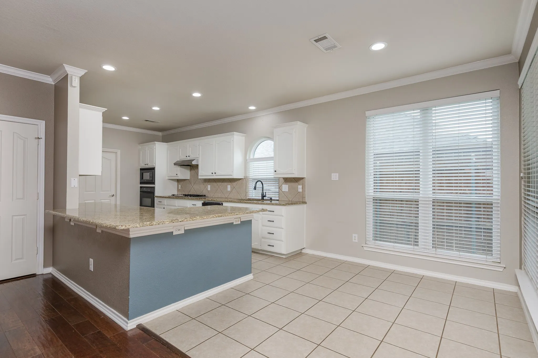 Spacious kitchen featuring an island with stone countertop, white cabinetry, integrated double ovens, and tile flooring