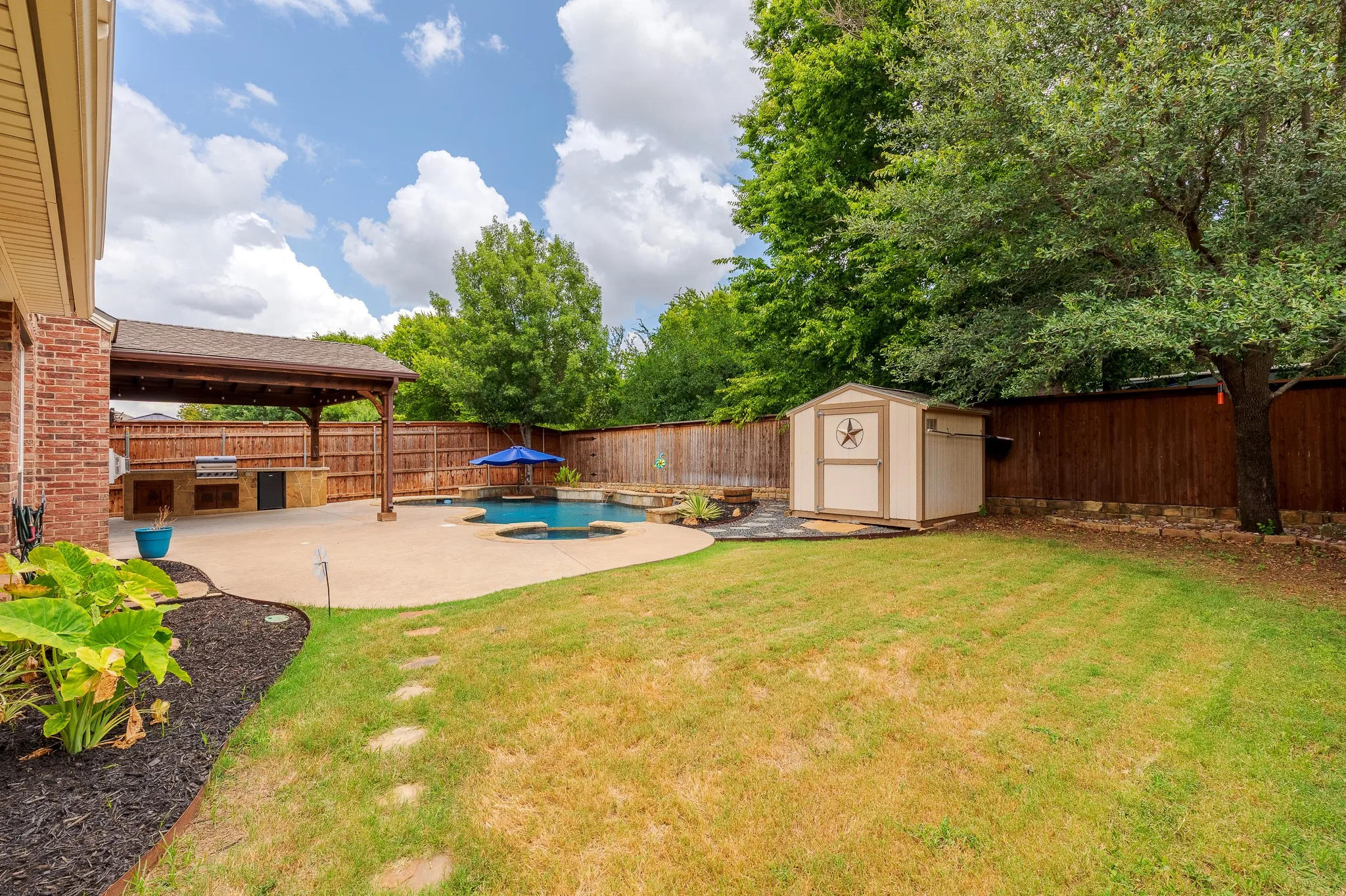 Expansive backyard featuring a custom pool, covered patio with an outdoor kitchen, wood fence, and a storage shed