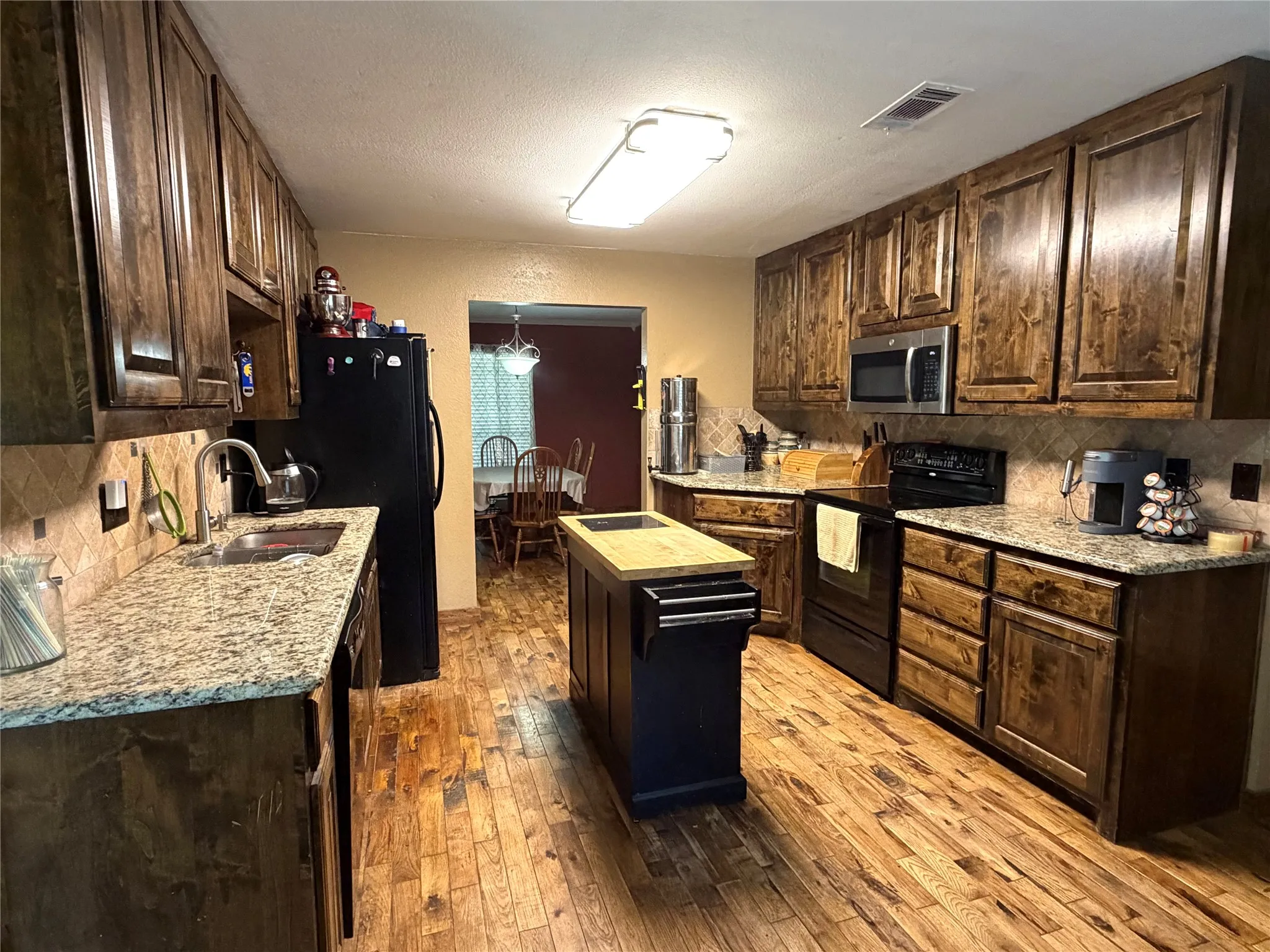 Kitchen featuring wood-finish flooring, wood cabinetry, granite-style countertops, stainless steel appliances, and an island with a butcher block top