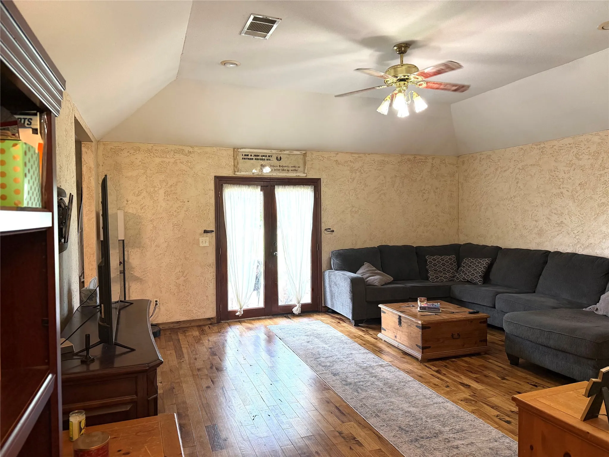 Vaulted ceiling living area featuring hardwood flooring, textured walls, and French doors