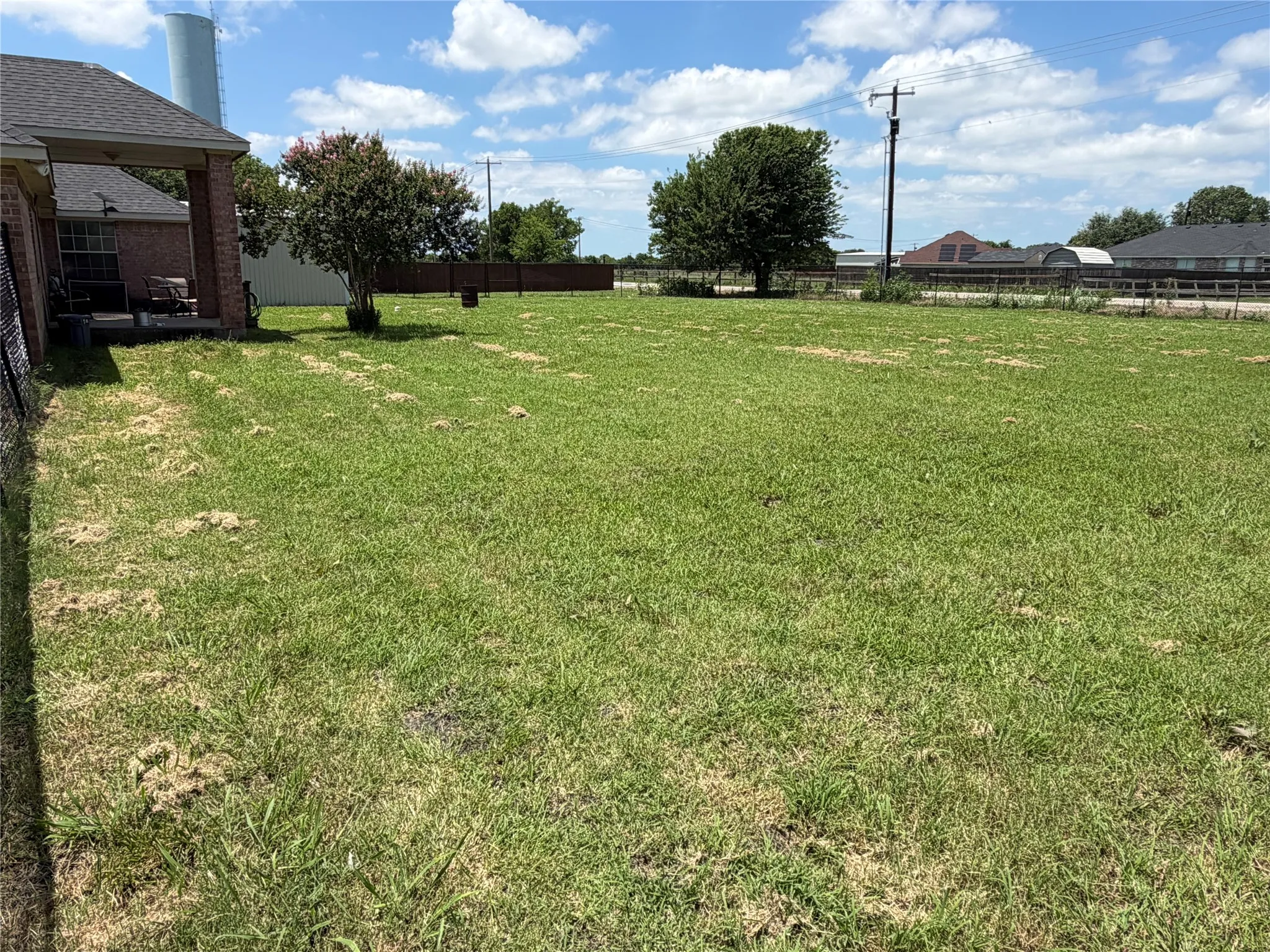 Expansive grassy yard with a covered patio area and mature trees