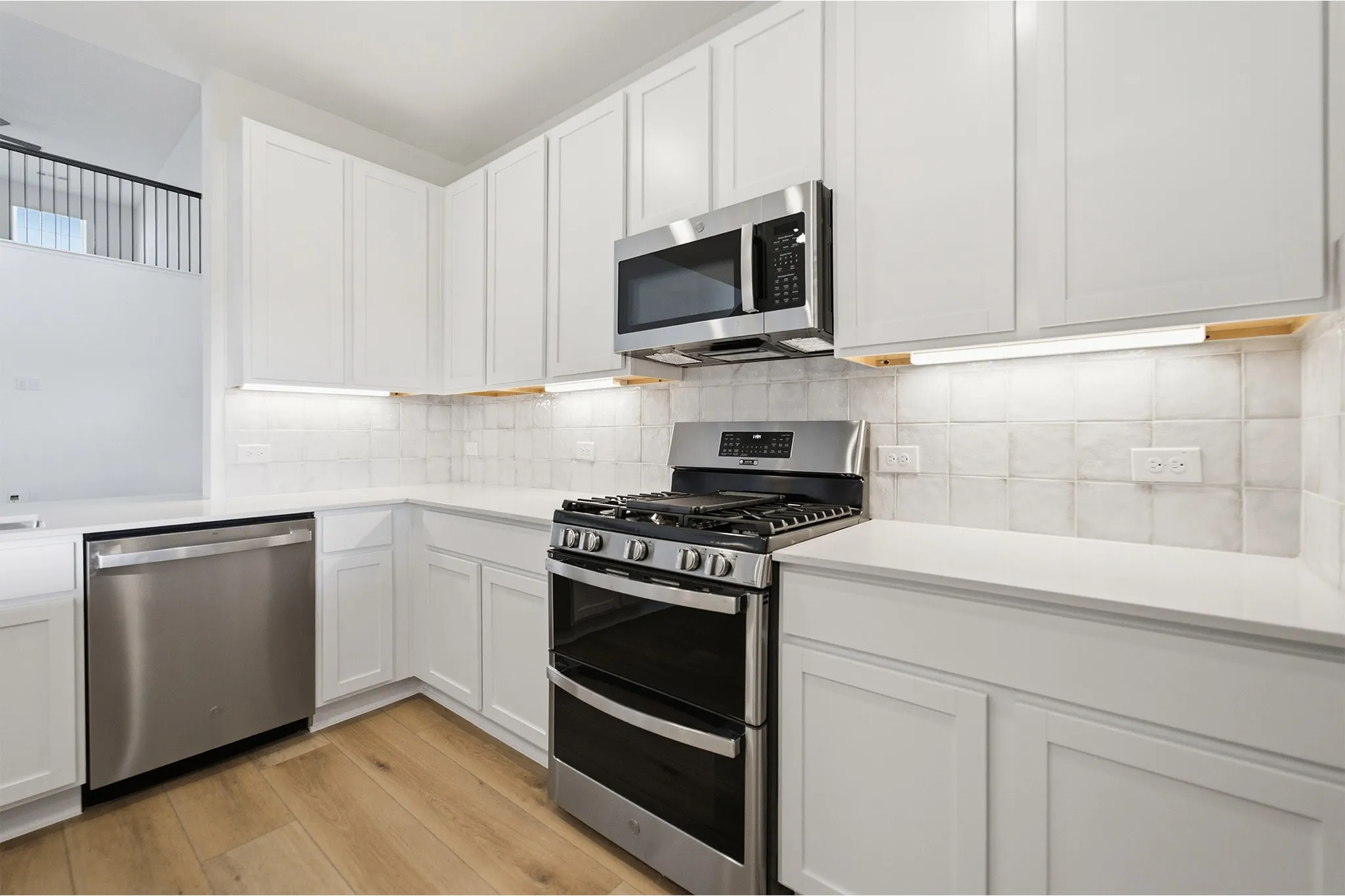 Modern kitchen featuring white shaker cabinetry, stainless steel appliances, light countertops, a tiled backsplash, and wood-finish flooring