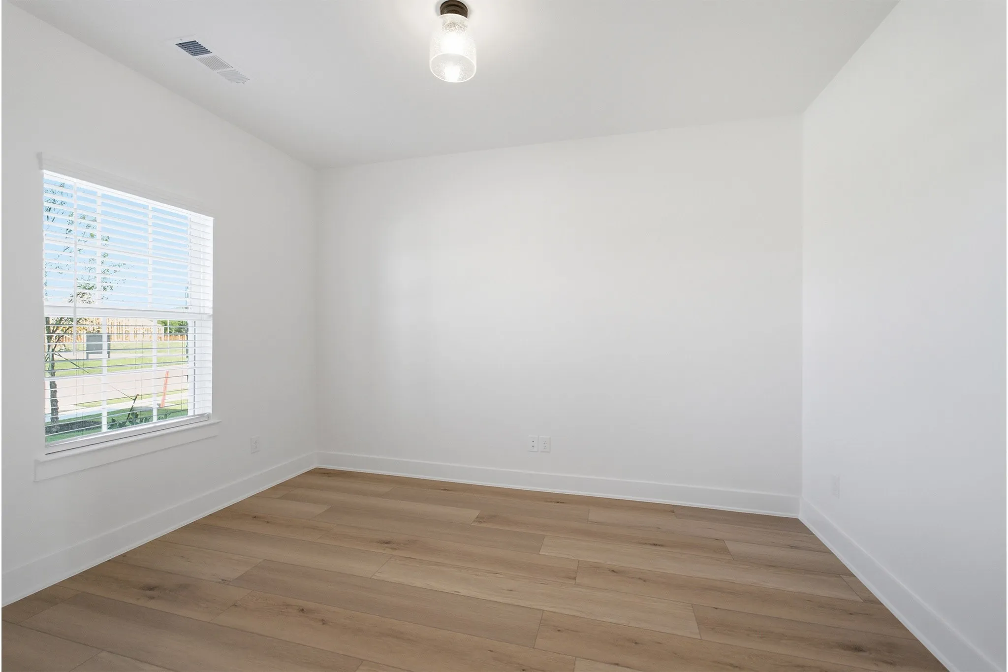 Bright interior room featuring wood-finish flooring, white baseboards, and a window with blinds
