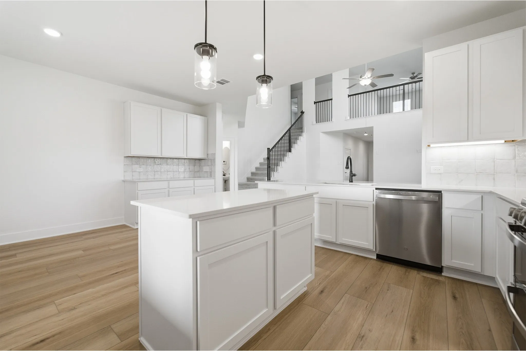 Contemporary kitchen featuring a central island, wood-finish flooring, white cabinetry, integrated stainless steel appliances, and a staircase with an open railing