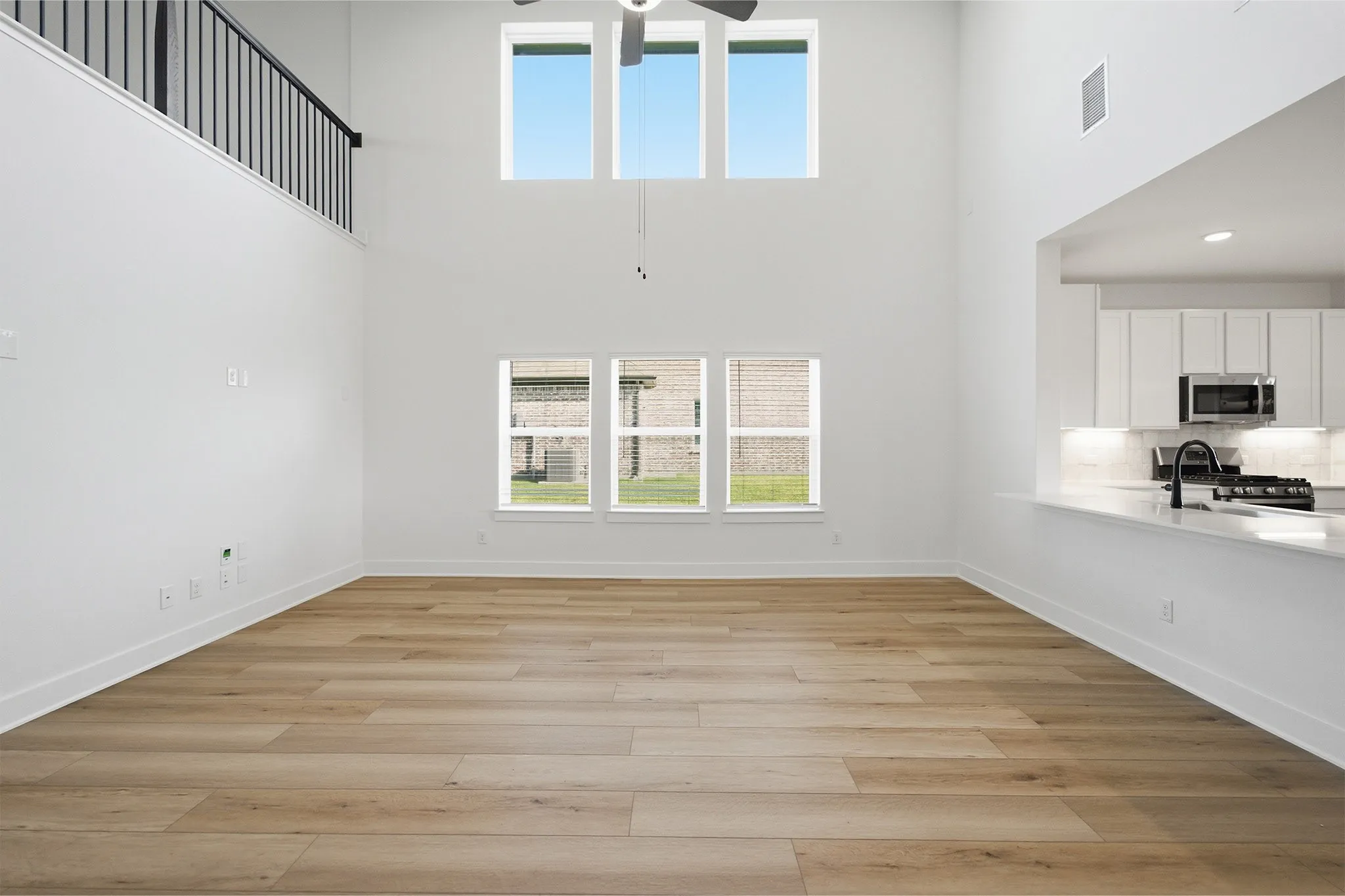 Vaulted living space with wood-finish flooring, a contemporary ceiling fan, and abundant natural light from upper and lower windows