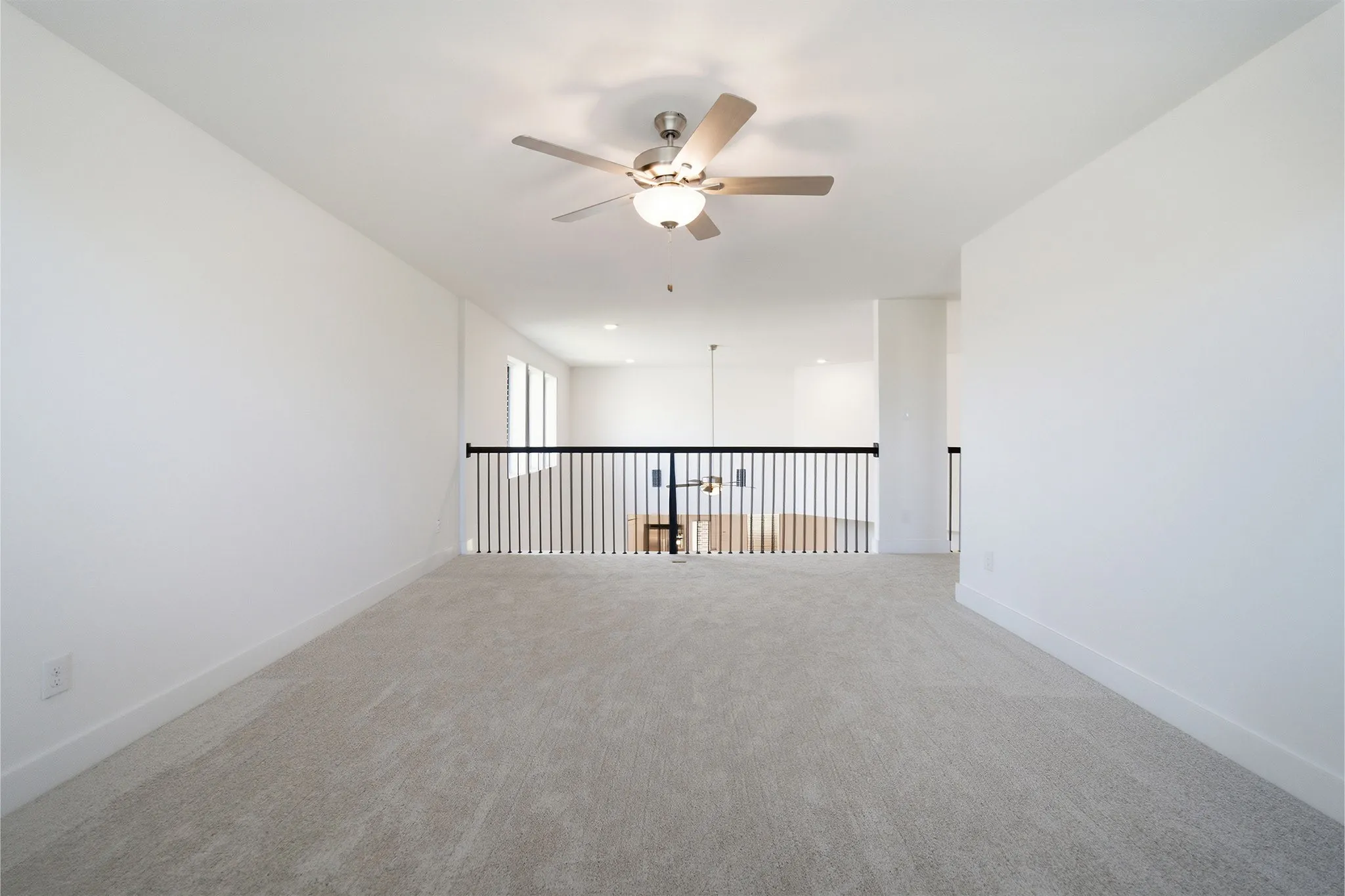 Carpeted loft space featuring a contemporary ceiling fan with light kit, a black metal spindle railing, and white baseboards
