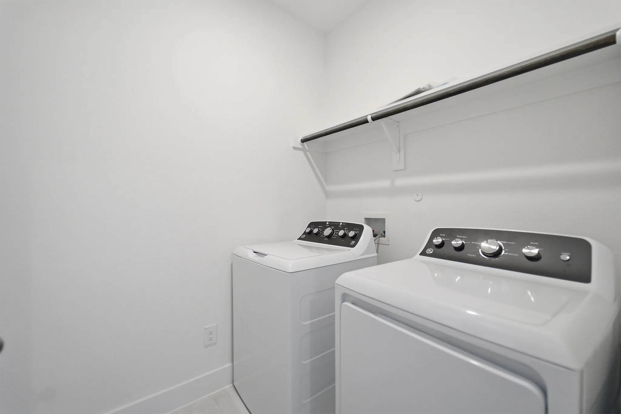 Dedicated laundry area featuring a white washer and dryer, a white wall shelf, and a dark clothing rod