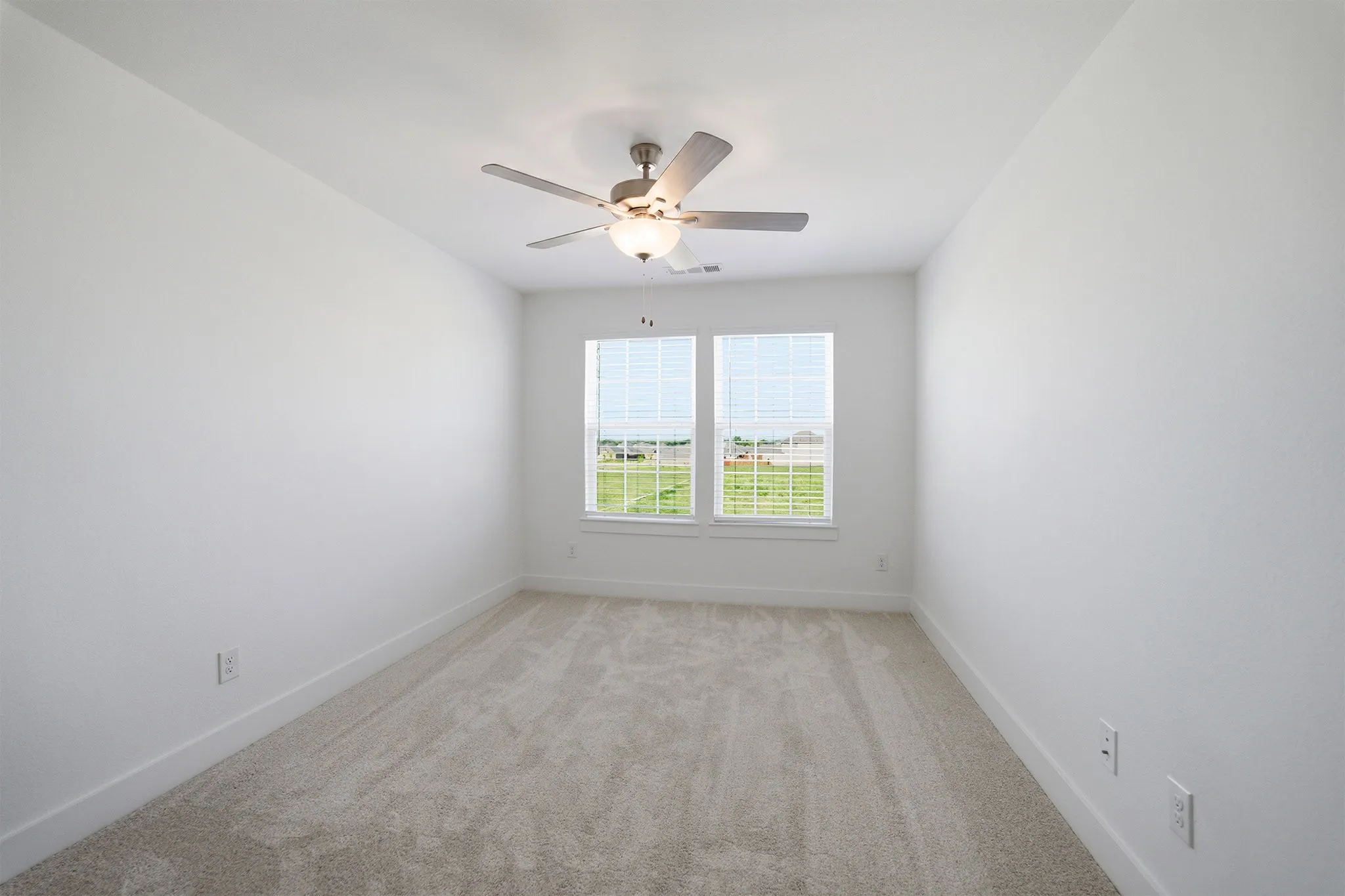 Bright room featuring two windows with blinds, carpeted flooring, a ceiling fan with integrated lighting, and white walls