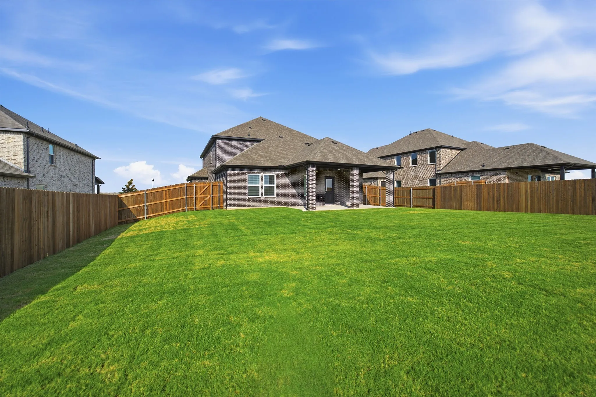 Expansive backyard featuring a manicured lawn, full privacy fencing, and a covered patio with brick columns