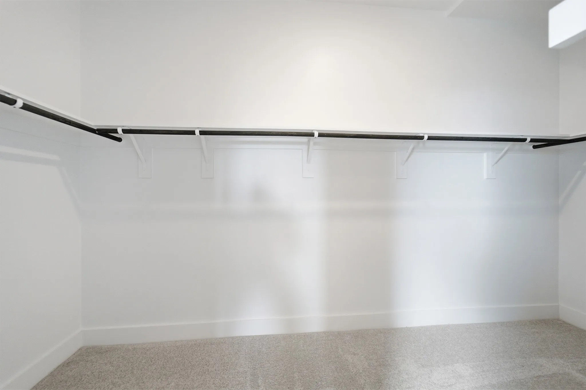 Expansive closet space featuring white walls, baseboards, and light-toned carpet flooring