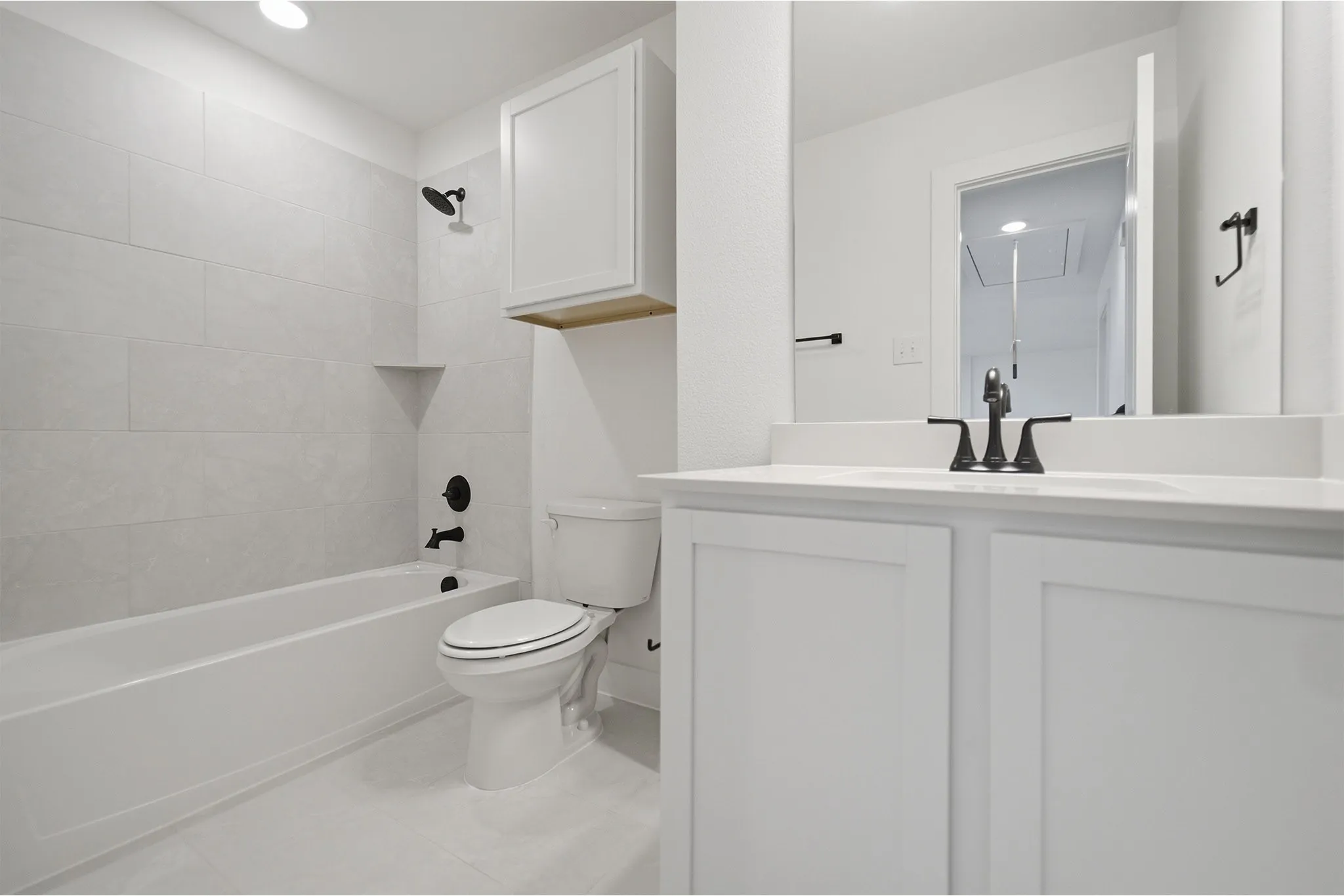 Bathroom featuring a white vanity with integrated sink, white cabinetry, dark bronze hardware, a white tub with subway tile surround, and a wall-mounted storage cabinet with a wood-finish shelf