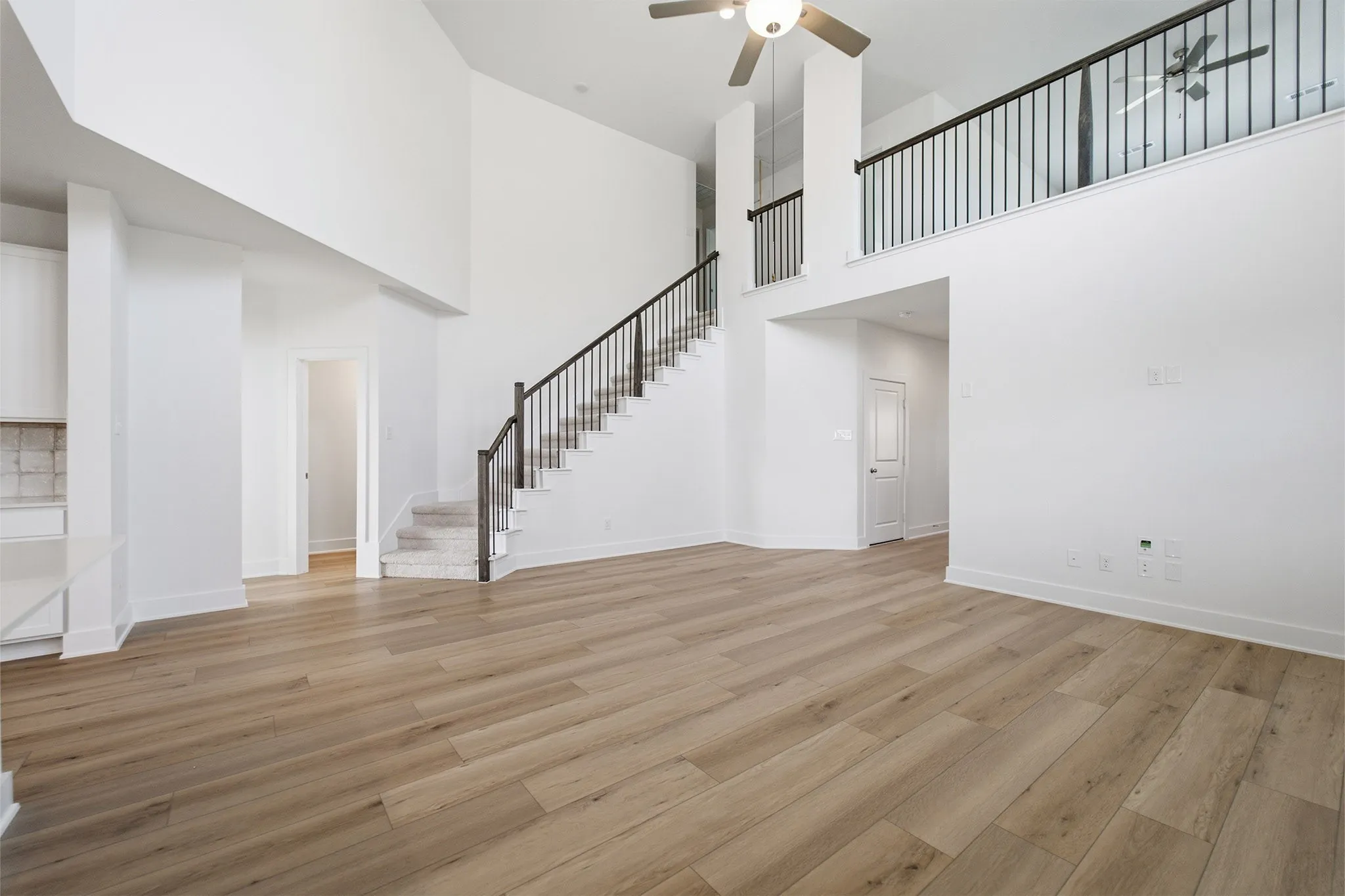 Spacious living area featuring high ceilings, wood-finish flooring, a two-story staircase with wrought iron balusters, an open loft area, and a ceiling fan with integrated lighting
