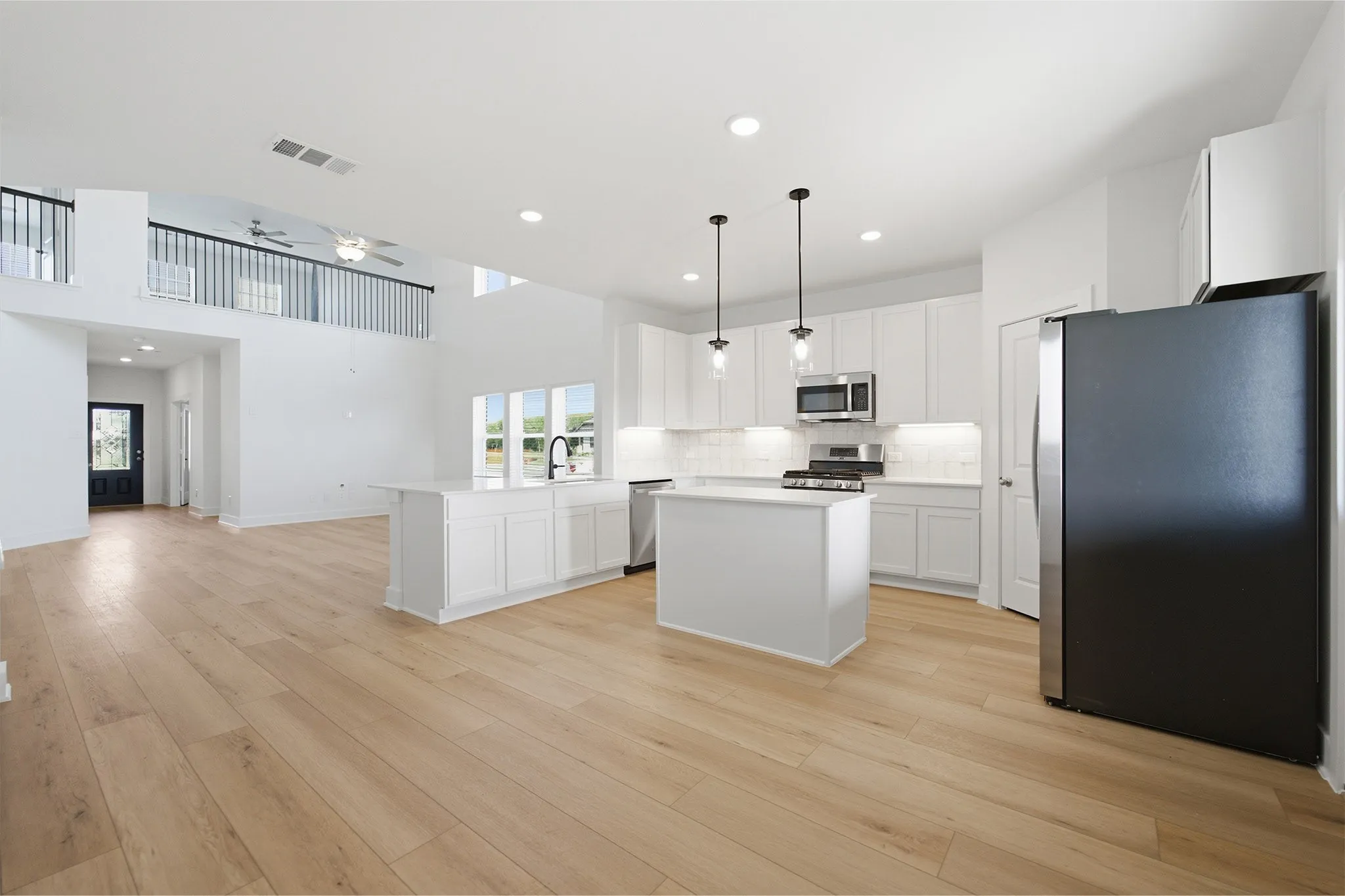 Open-concept living space featuring a modern kitchen with a large island, white cabinetry, stainless steel appliances, and pendant lighting