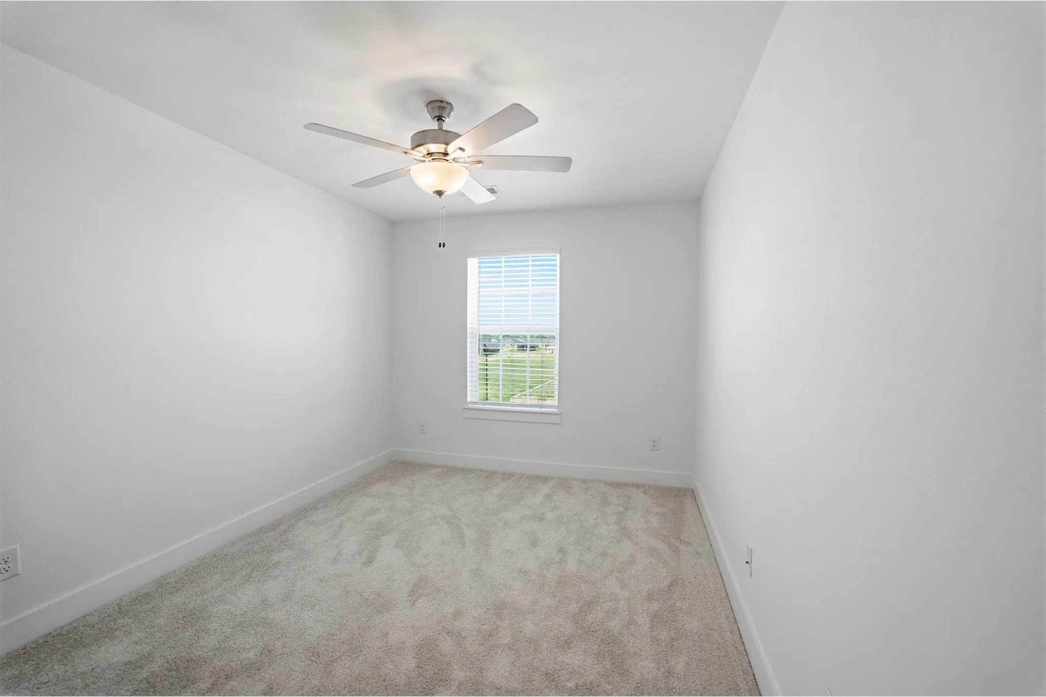 Bright room featuring a ceiling fan with integrated lighting, a single window with blinds, light-colored carpeting, and white baseboards