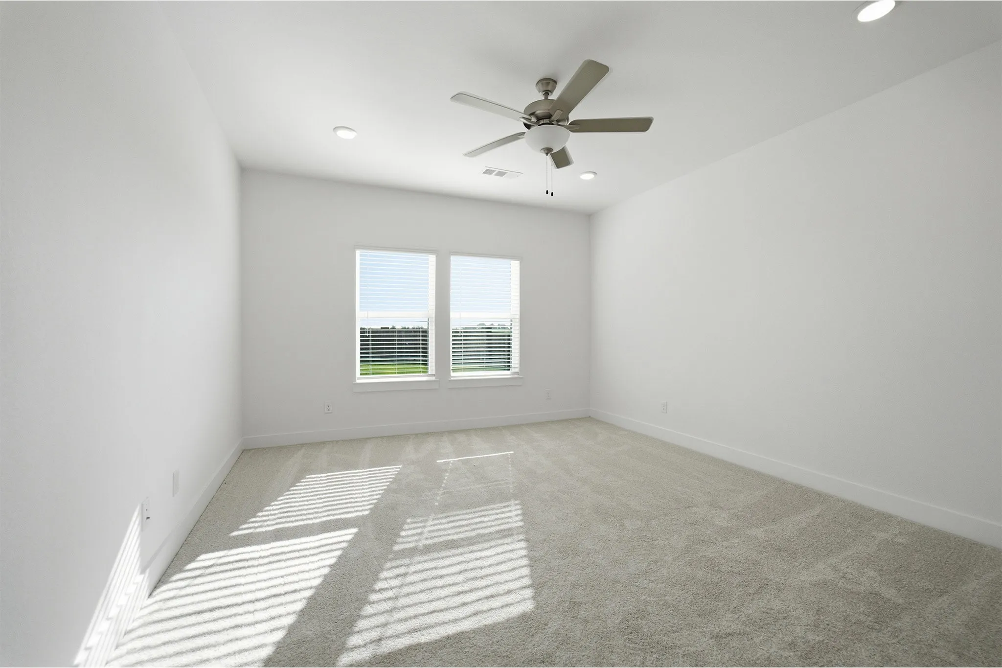 Spacious room with light gray carpeting, neutral white walls, and a ceiling fan with integrated lighting