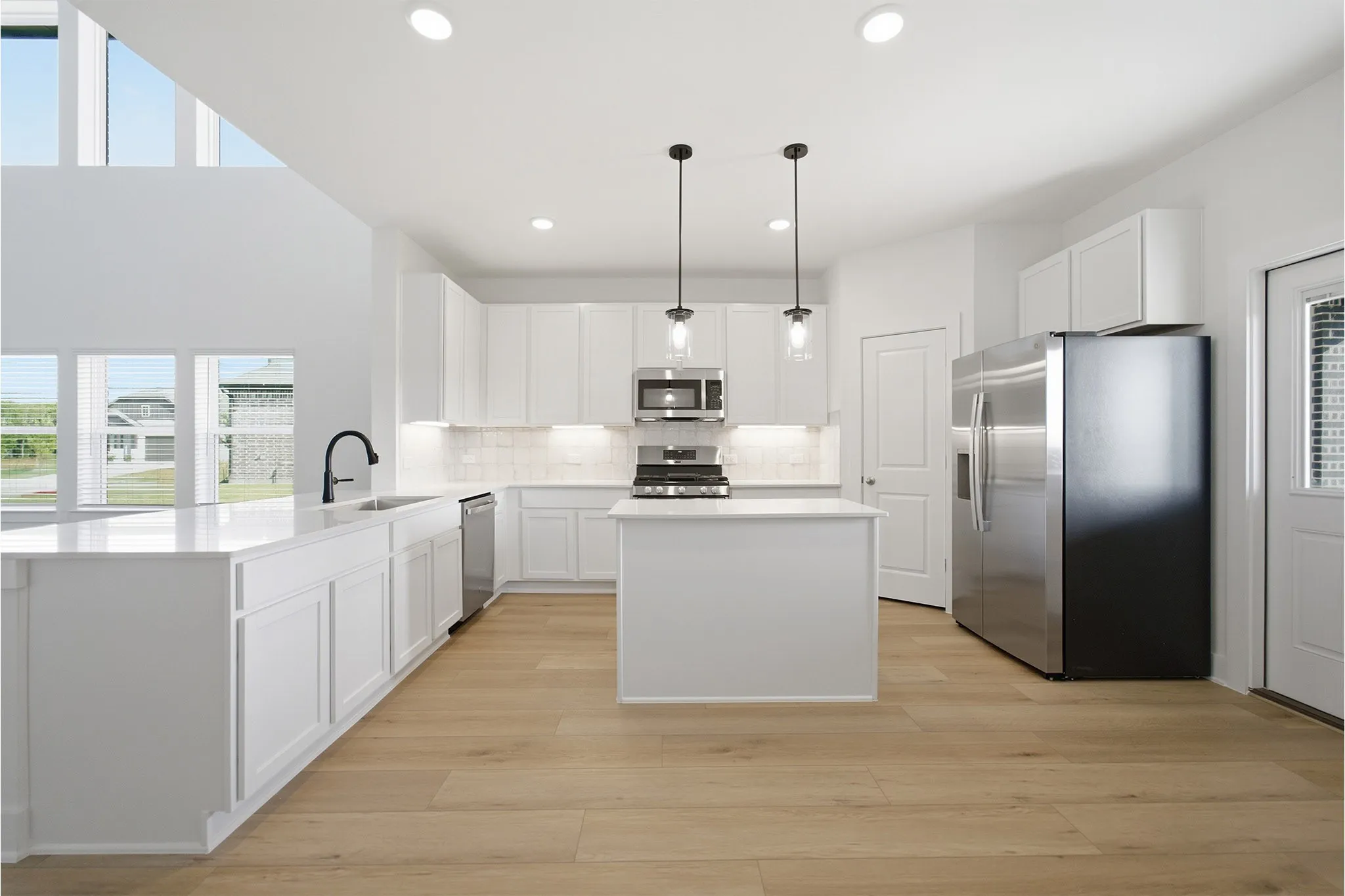 Modern kitchen featuring white cabinetry, light countertops, wood-finish flooring, stainless steel appliances, and a central island