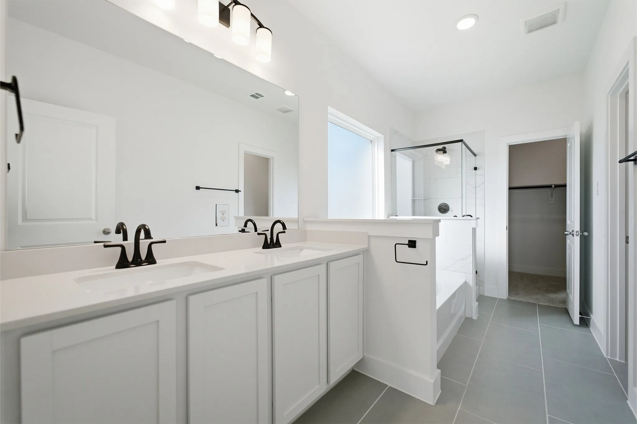Spacious bathroom featuring a dual vanity with white cabinetry and countertops, a large mirror, a glass-enclosed shower, and gray floor tiling
