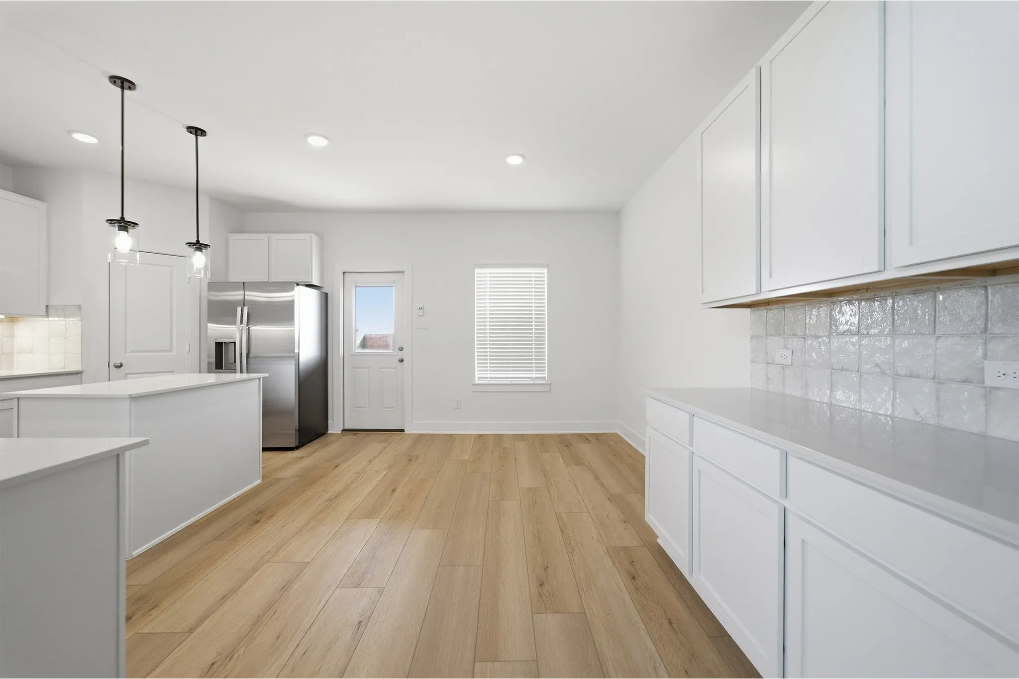 Modern kitchen featuring white shaker cabinetry, light wood-finish flooring, recessed lighting, and a stainless steel refrigerator