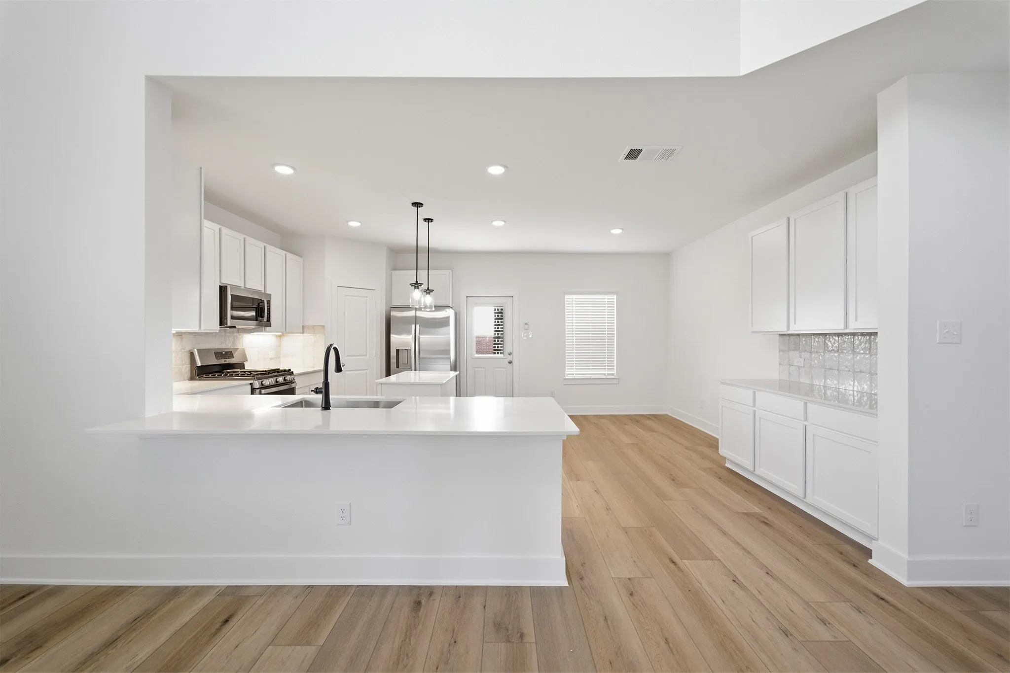 Open concept living space featuring a kitchen with white cabinetry, stainless steel appliances, and an island with a sink and pendant lighting