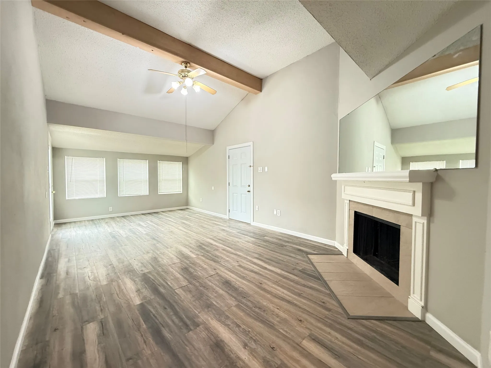 Spacious living area featuring vaulted ceilings with exposed wood beams, wood-finish flooring, a ceiling fan, and multiple windows with blinds