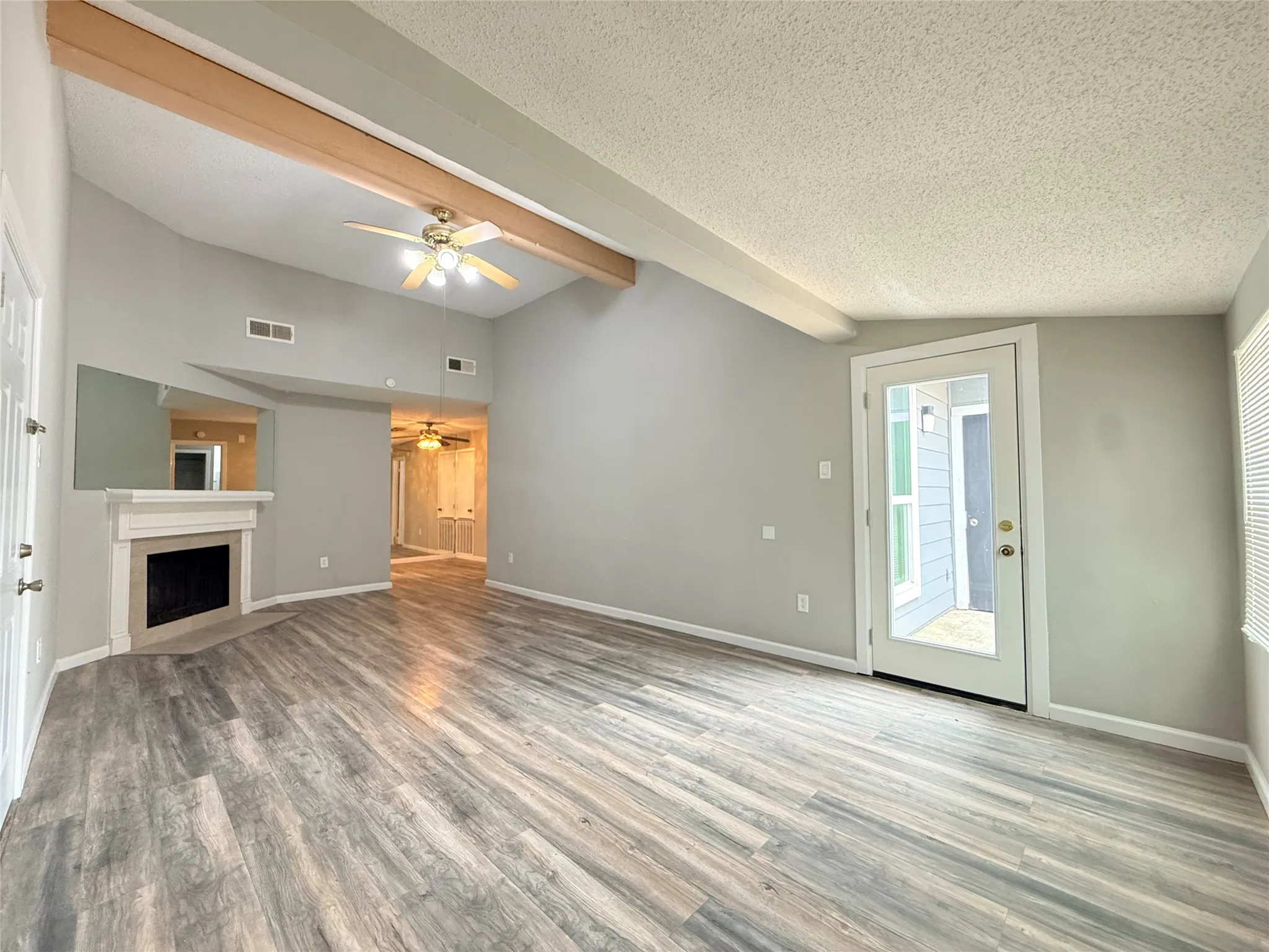 Spacious living area featuring wood-finish flooring, a fireplace with a mantel, and a vaulted ceiling with exposed beams