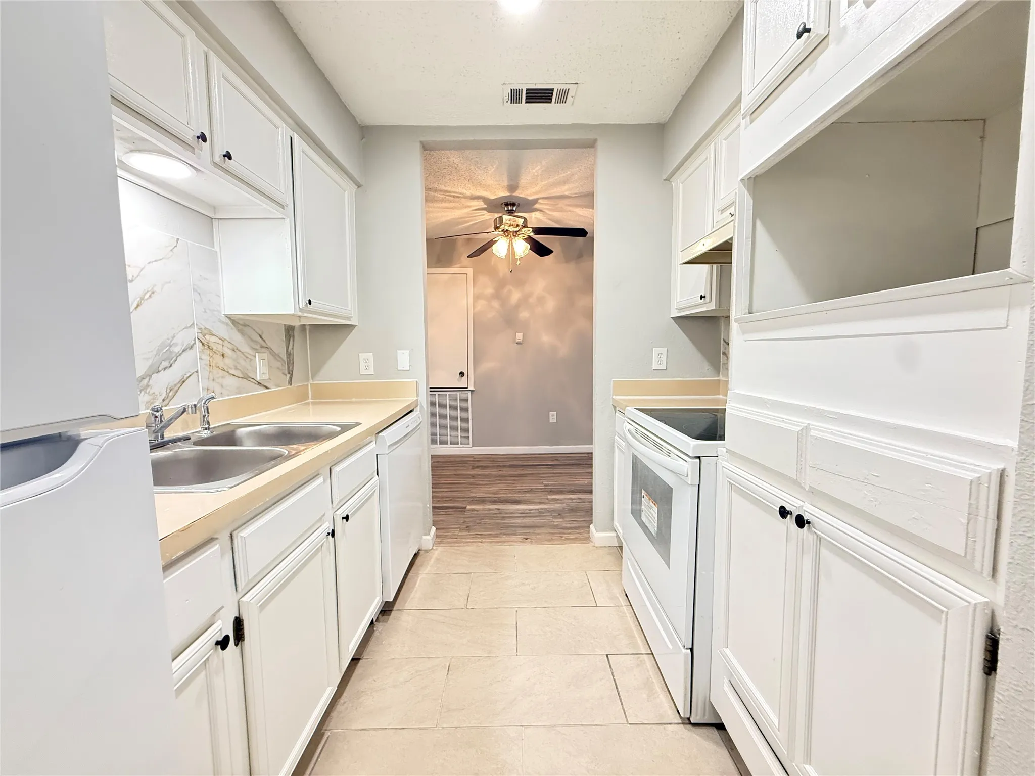 Galley kitchen featuring white cabinetry, light-toned countertops, a double basin stainless steel sink, a white electric range, and tile flooring