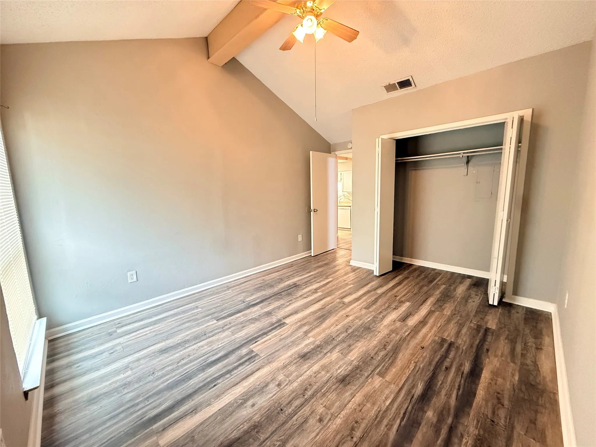 Vaulted ceiling room featuring wood-finish flooring, a ceiling fan, and a bi-fold door closet with shelving