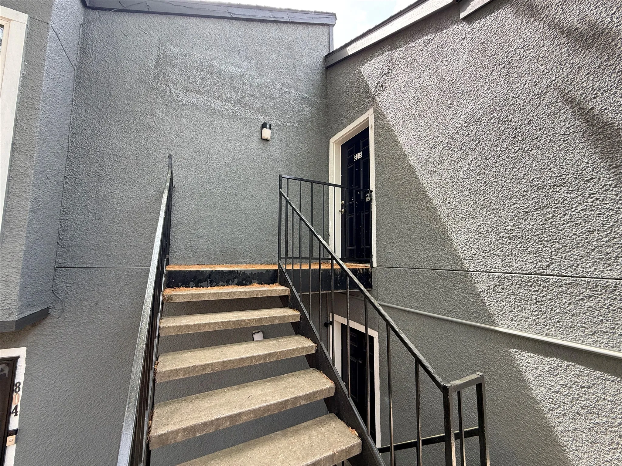 Exterior stairway with concrete treads and black metal railings, leading to a dark entry door with white trim