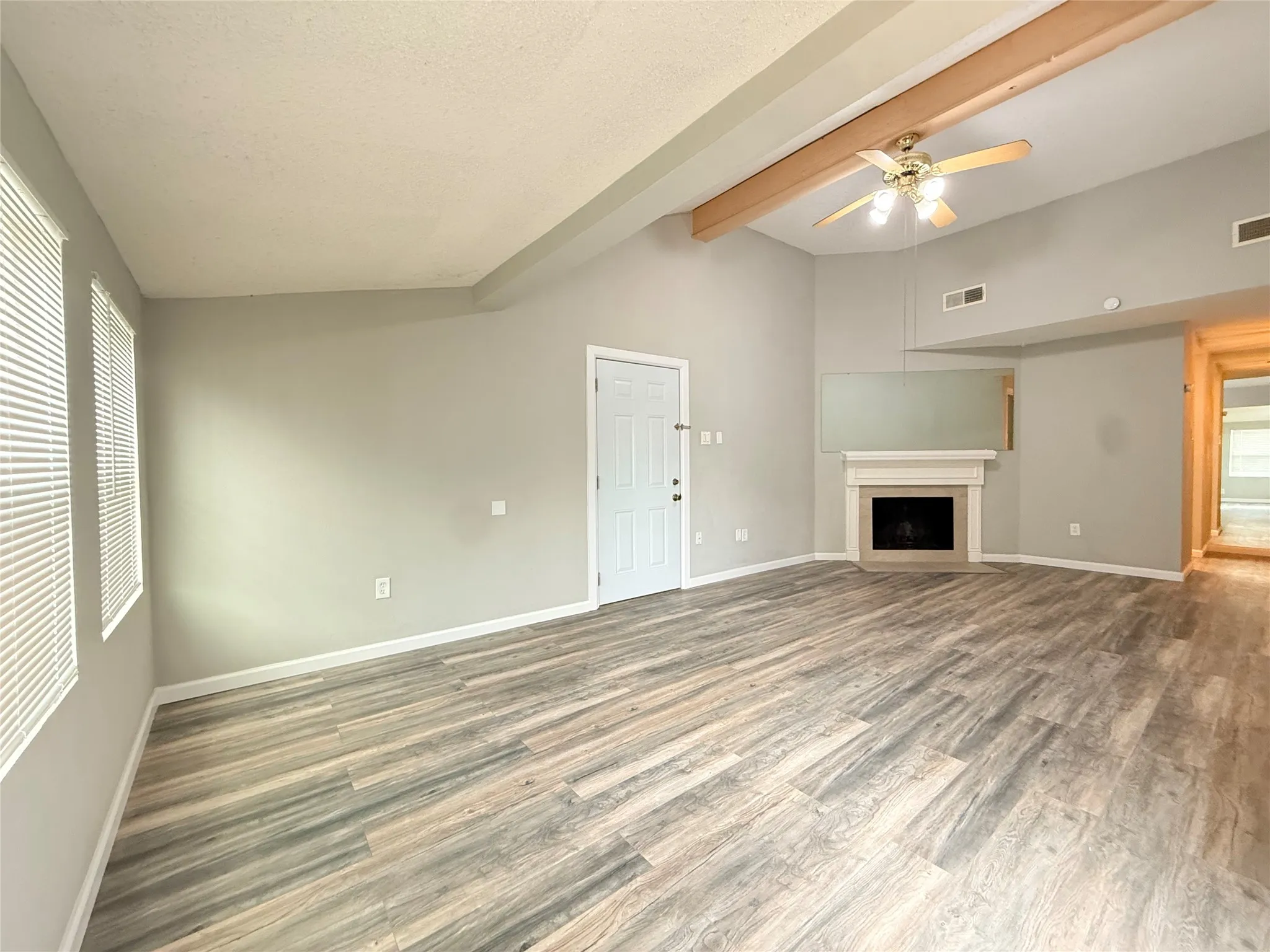 Spacious living area featuring wood-finish flooring, a fireplace with a mantel, vaulted ceilings with exposed beams, and a ceiling fan
