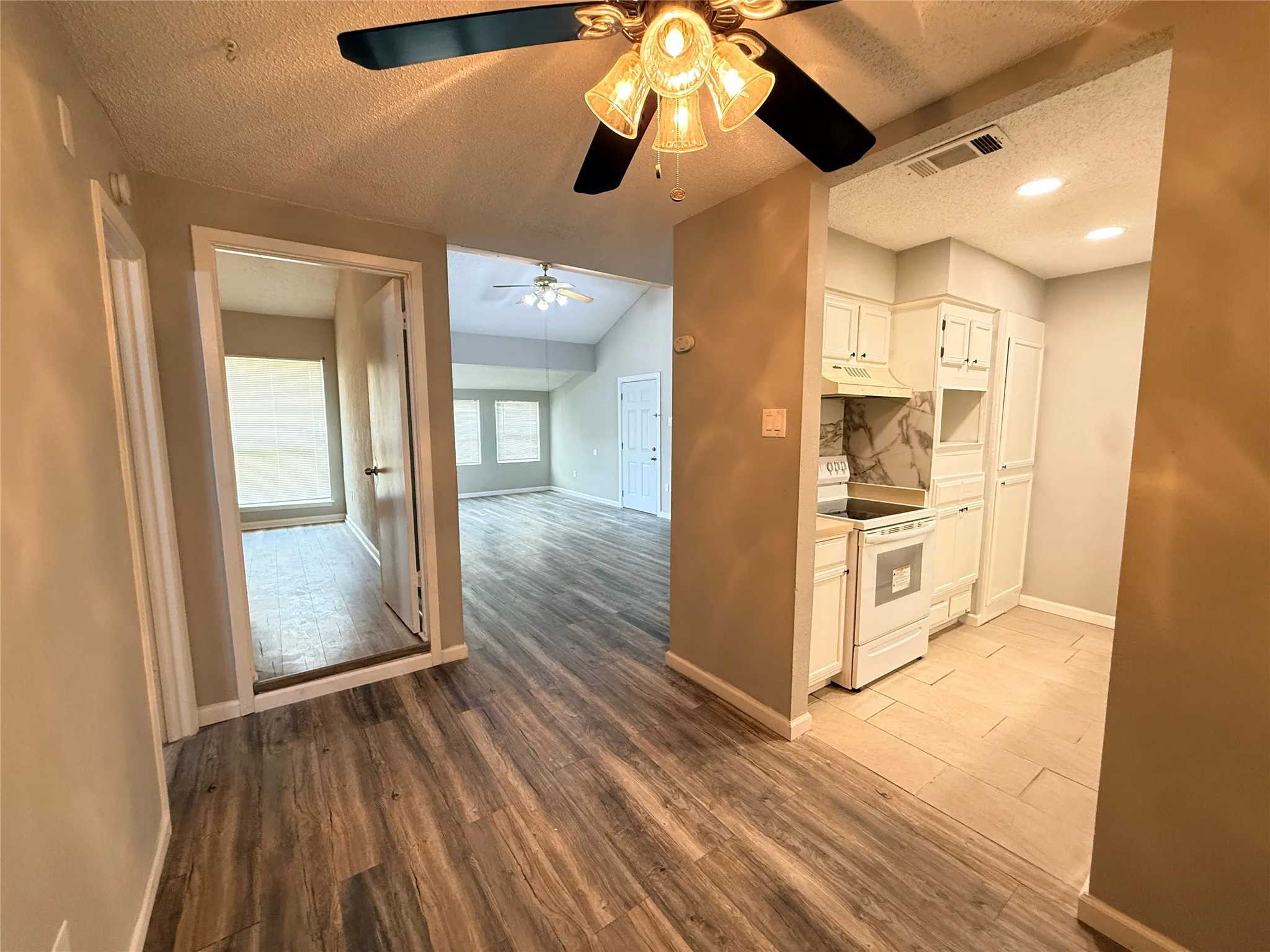 Open-concept living space with wood-finish flooring, vaulted ceilings, and a kitchen featuring white cabinetry, a built-in electric range, and a tiled backsplash