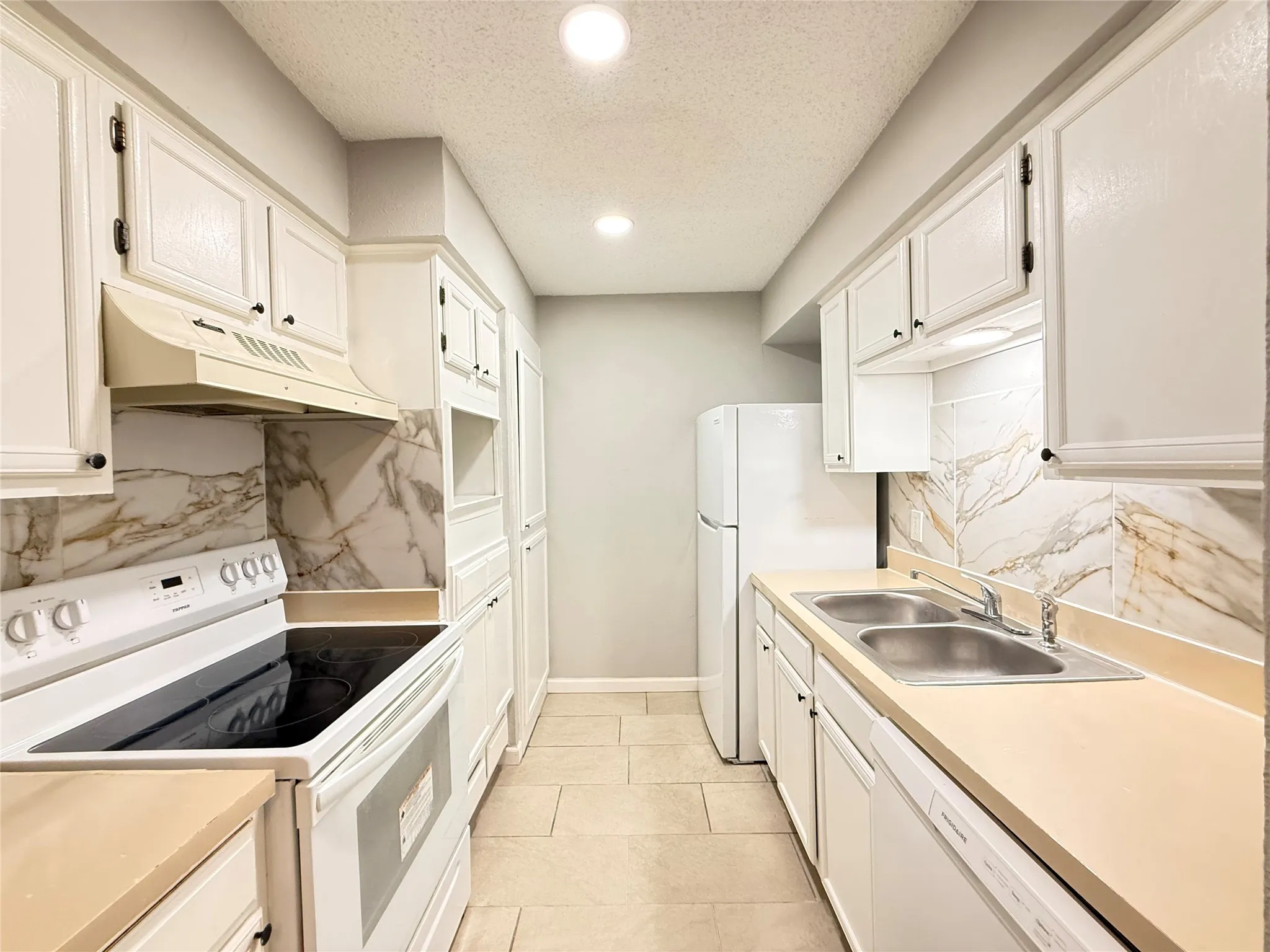 Galley kitchen featuring white cabinetry, light countertops, integrated white appliances, a tile backsplash with veining, and tile flooring